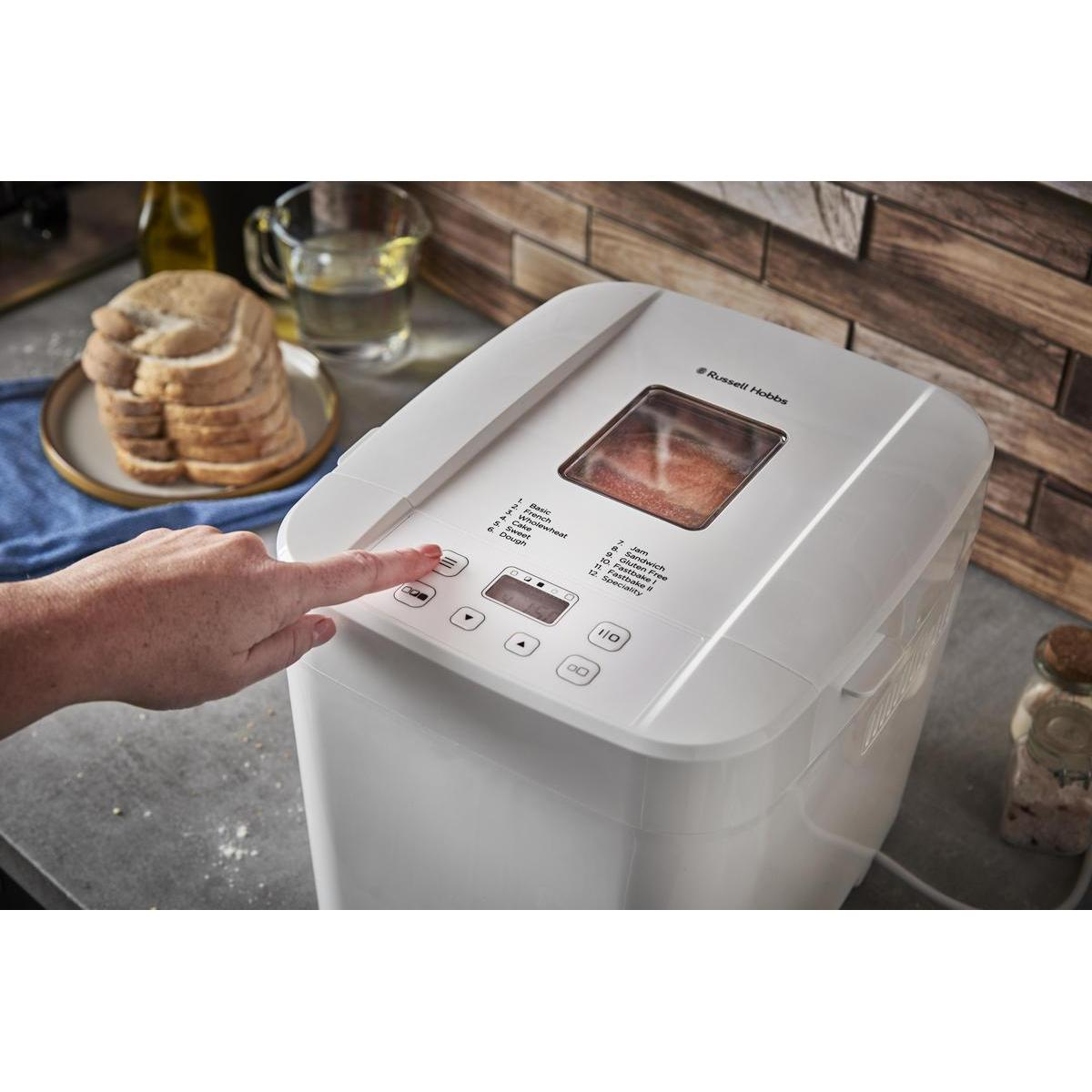 Ręka osoby naciskająca przycisk na białej maszynie do robienia chleba.