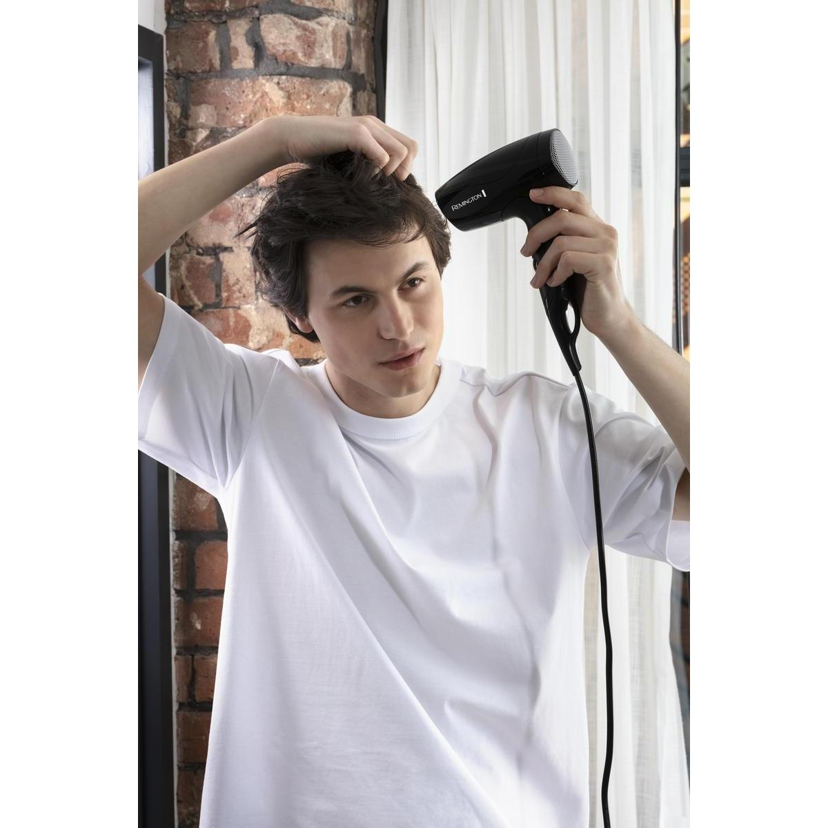 Uomo che si asciuga i capelli con un asciugacapelli nero. Indossa una maglietta bianca.