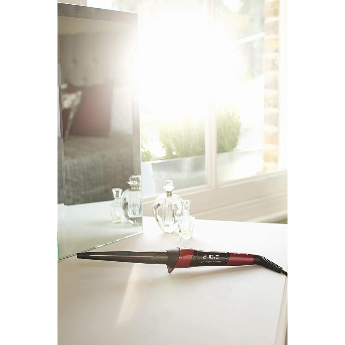 Lockenstab auf weißem Tisch. Spiegel, Parfümflaschen im Hintergrund sichtbar.