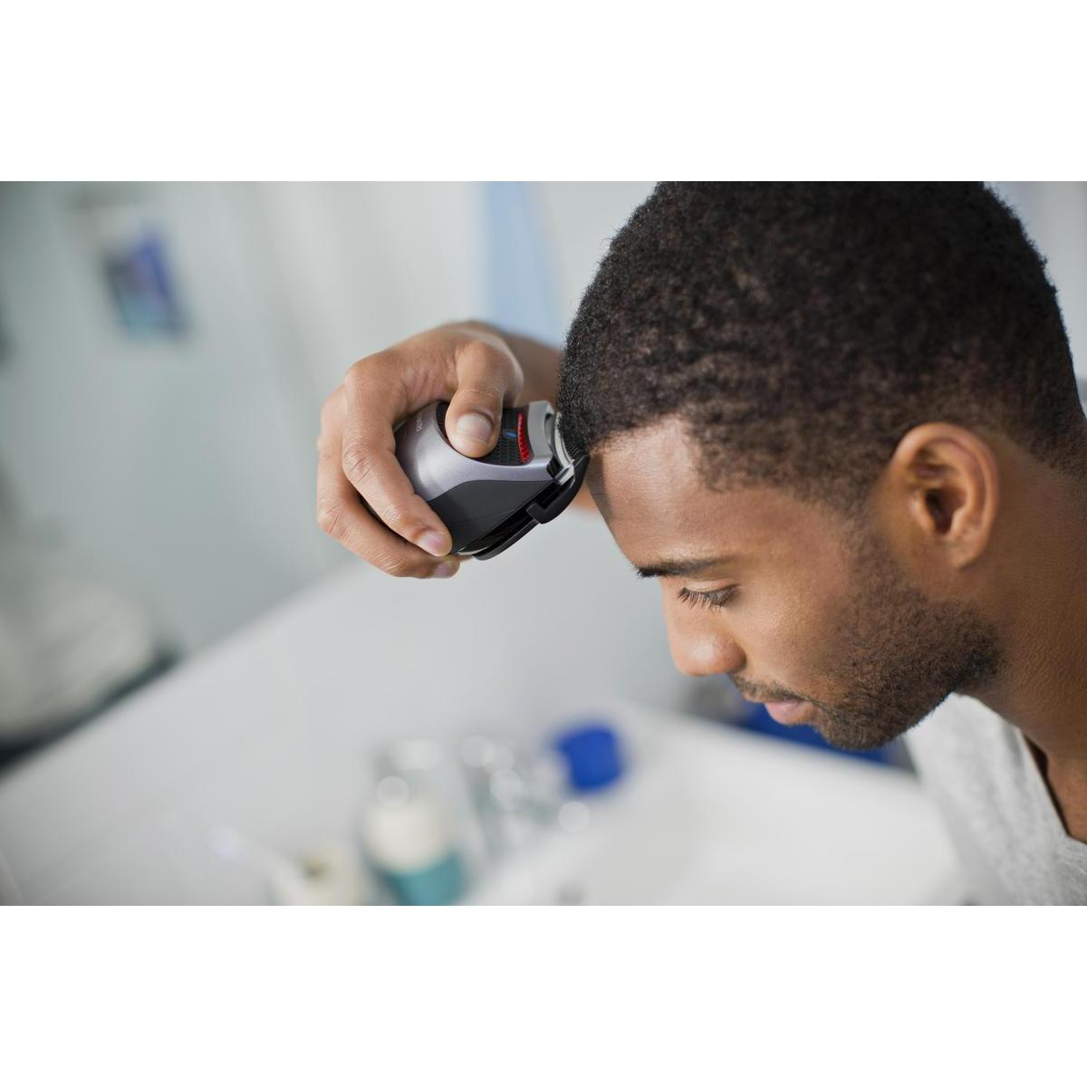 Mężczyzna goli głowę golarką elektryczną. Spogląda w dół w łazience.