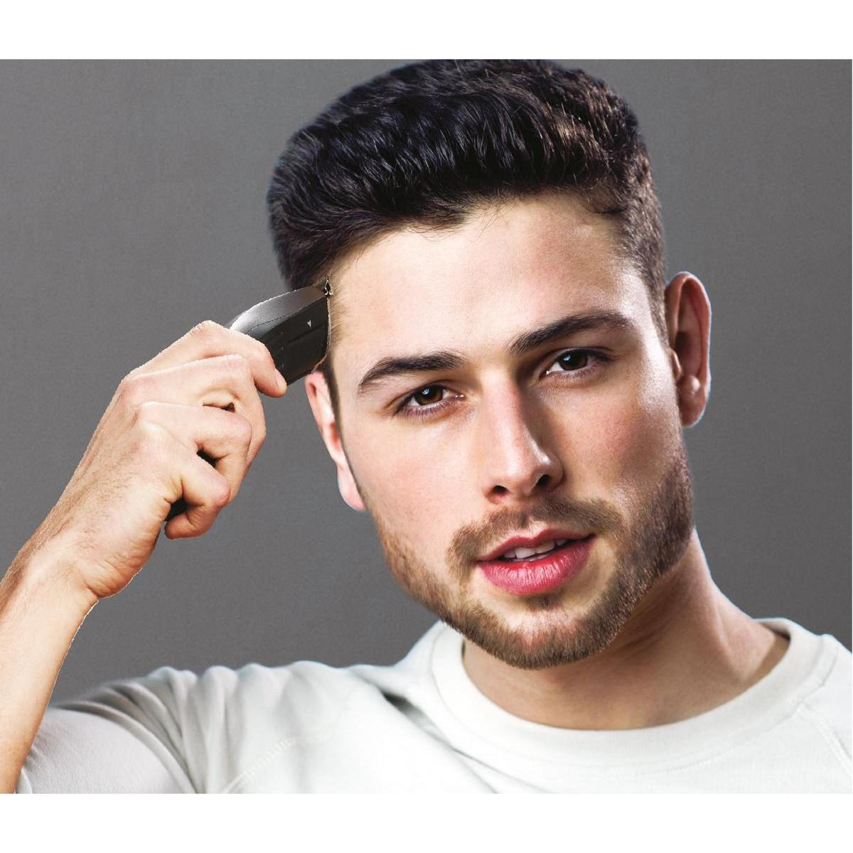 Mężczyzna obcina włosy czarną maszynką, patrzy w kamerę.