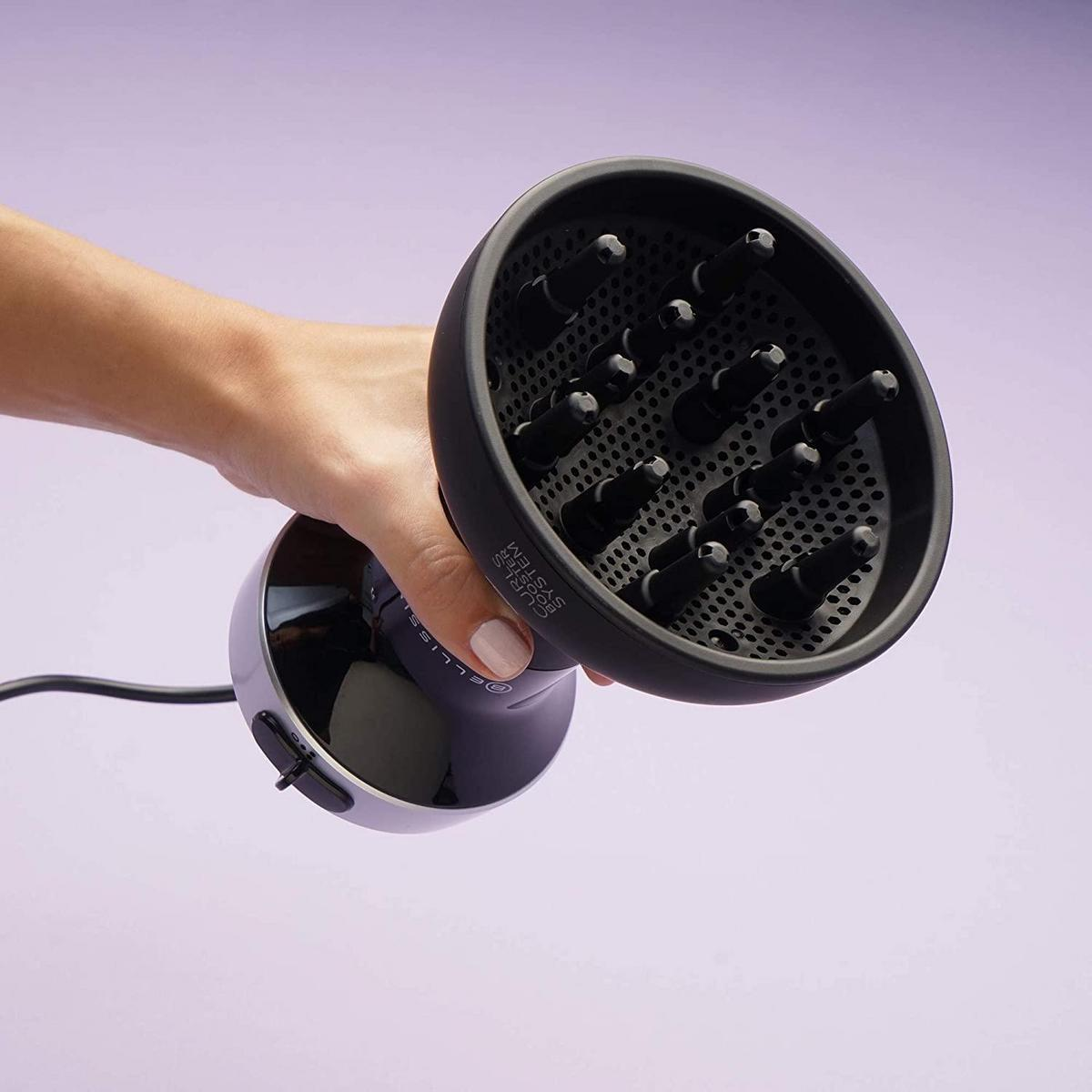 Mano che tiene un diffusore nero per asciugacapelli su sfondo viola. Diffusore con molti ugelli.