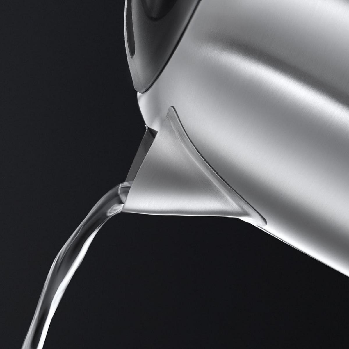 Water pouring from a silver kettle against a black background, showing the spout and water flow.