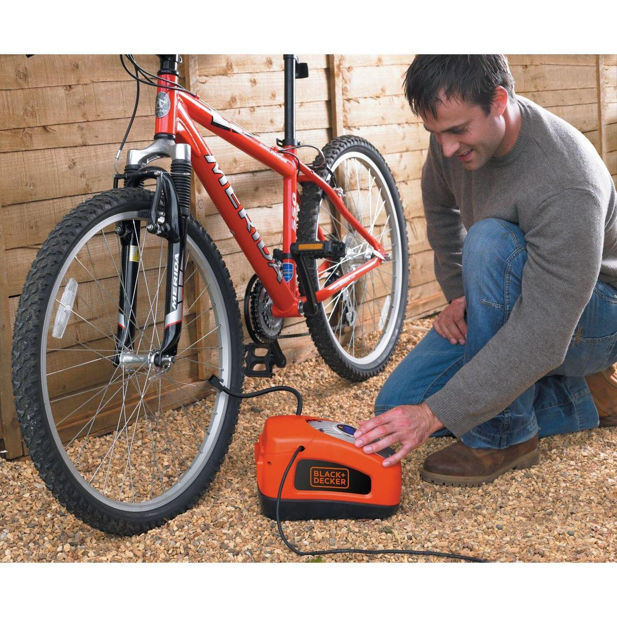 Ein Mann pumpt einen Fahrradreifen mit einer orangenen Black & Decker Pumpe auf.