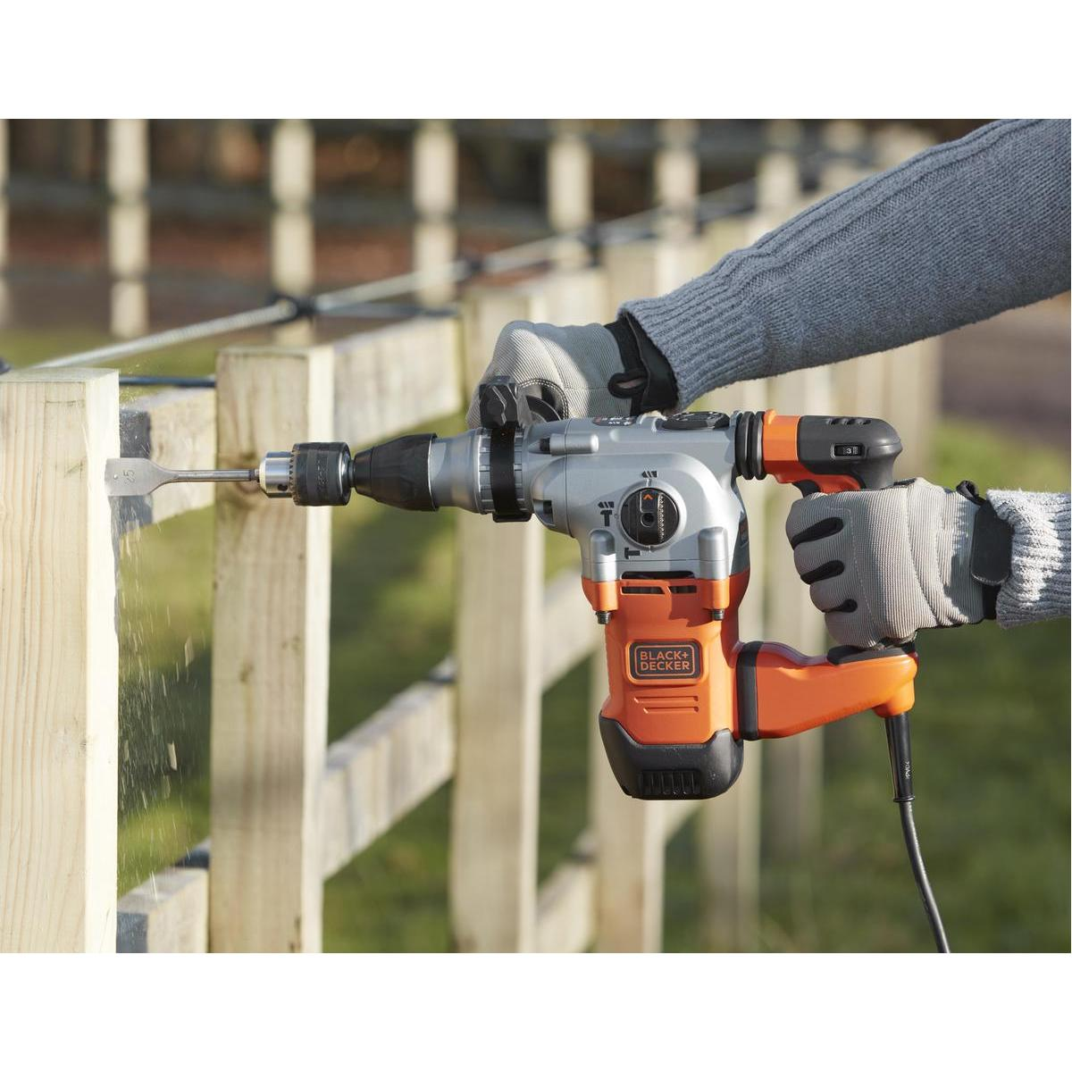 Person verwendet einen Black & Decker Bohrer, um in einen Holzzaun zu bohren. Orange und graue Farben.
