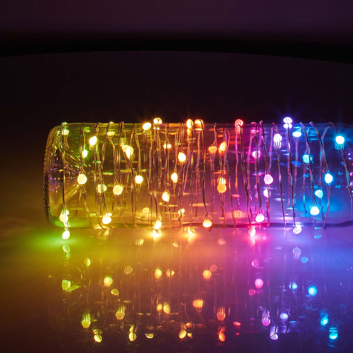 Una bottiglia di vetro con luci colorate all'interno, su una superficie riflettente.
