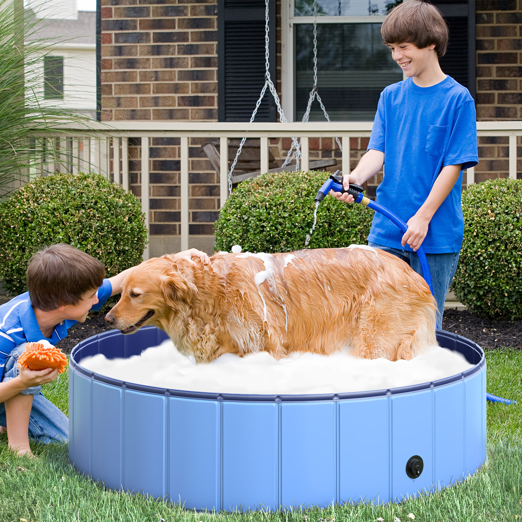 Due ragazzi lavano un golden retriever in una piscina di plastica blu in un cortile.
