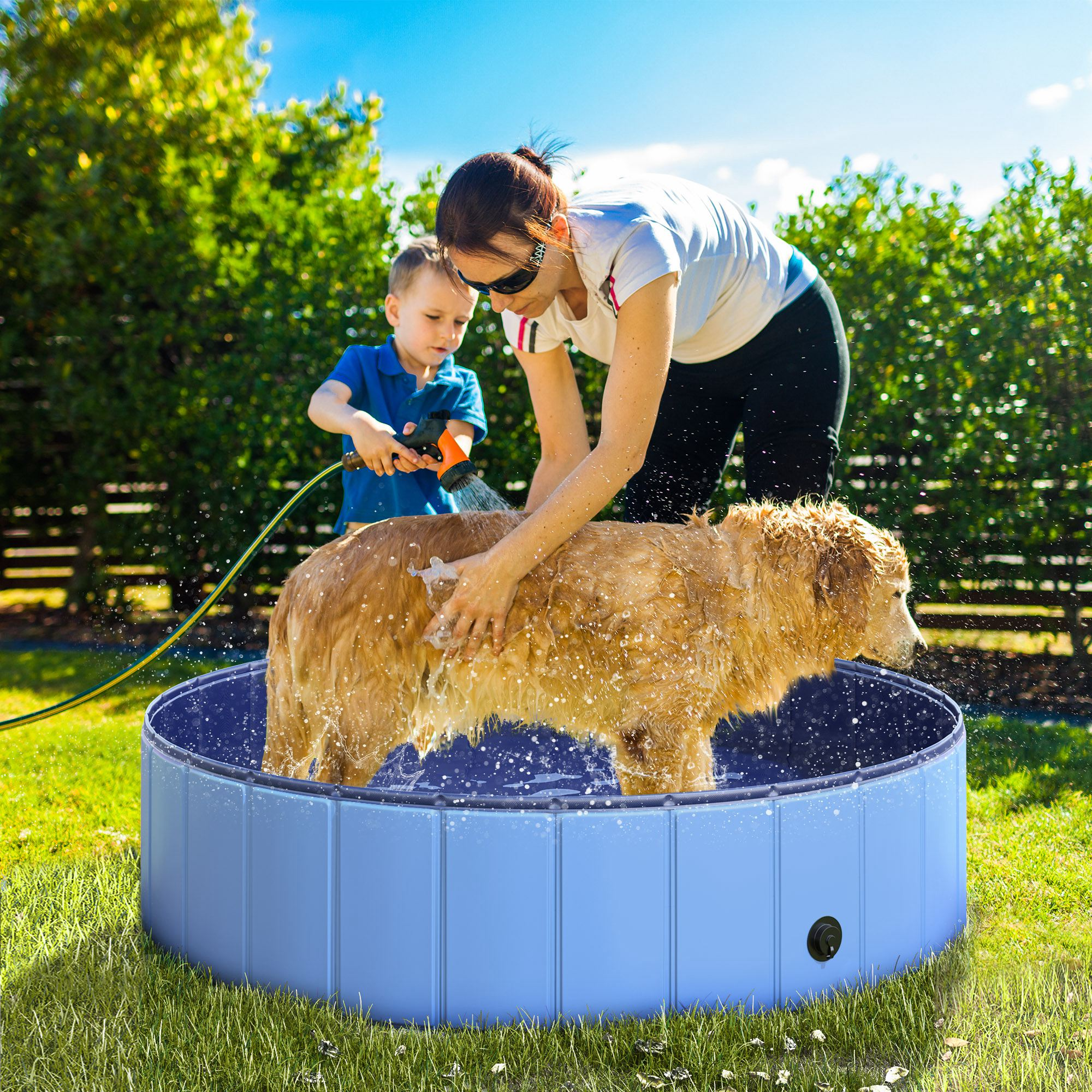 Una donna e un bambino lavano un golden retriever in una piscina blu per cani sull'erba verde.