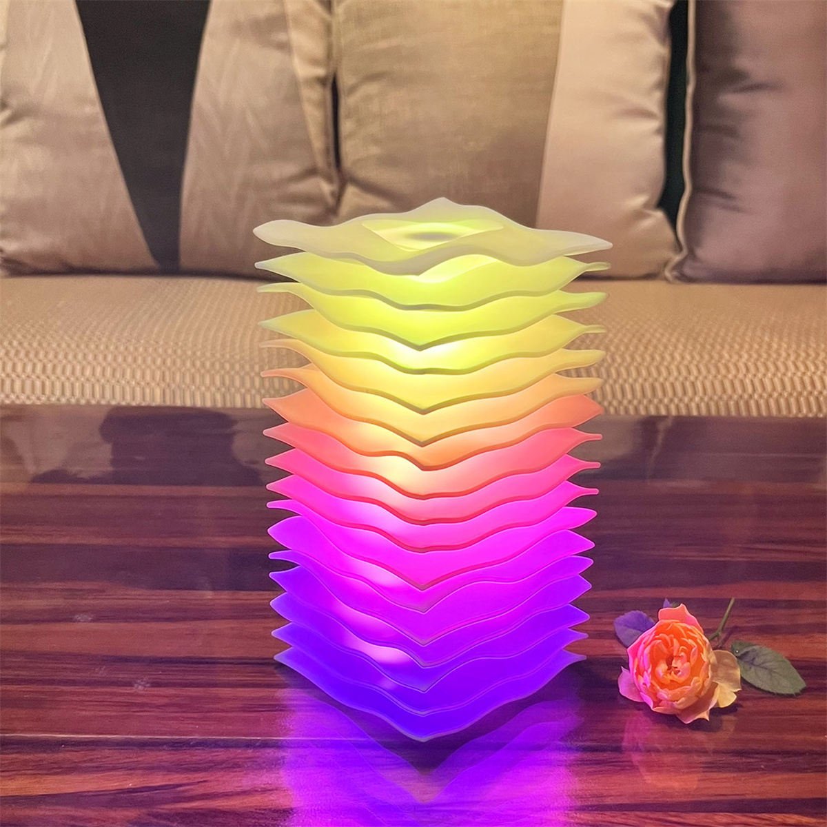 Beleuchtete, geschichtete Lampe mit Farbverlauf, lila bis gelb. Rose und Sofa im Hintergrund.