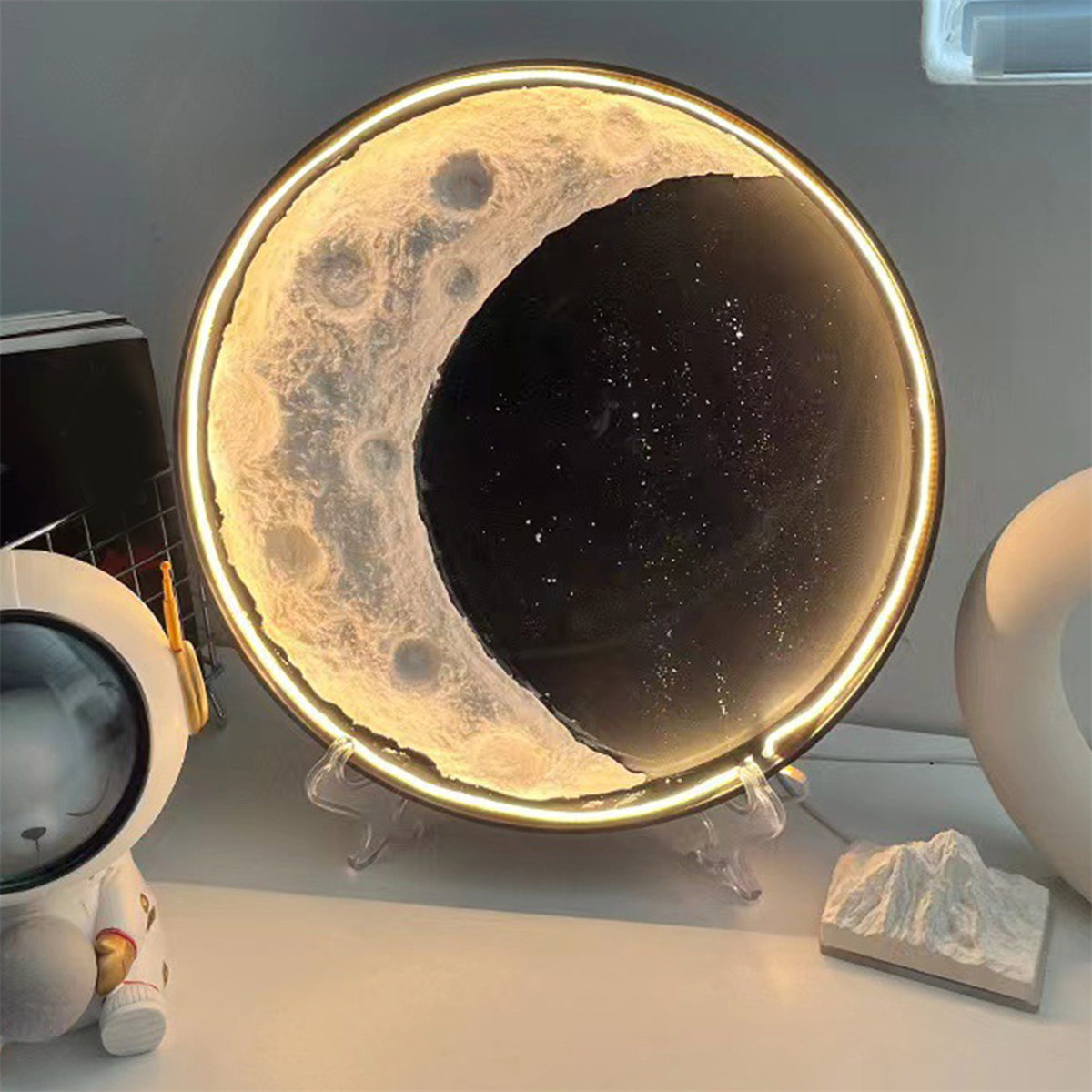 Eine mondförmige Lampe mit sternenklarem dunklem Hintergrund, auf einem Tisch mit dekorativen Objekten.