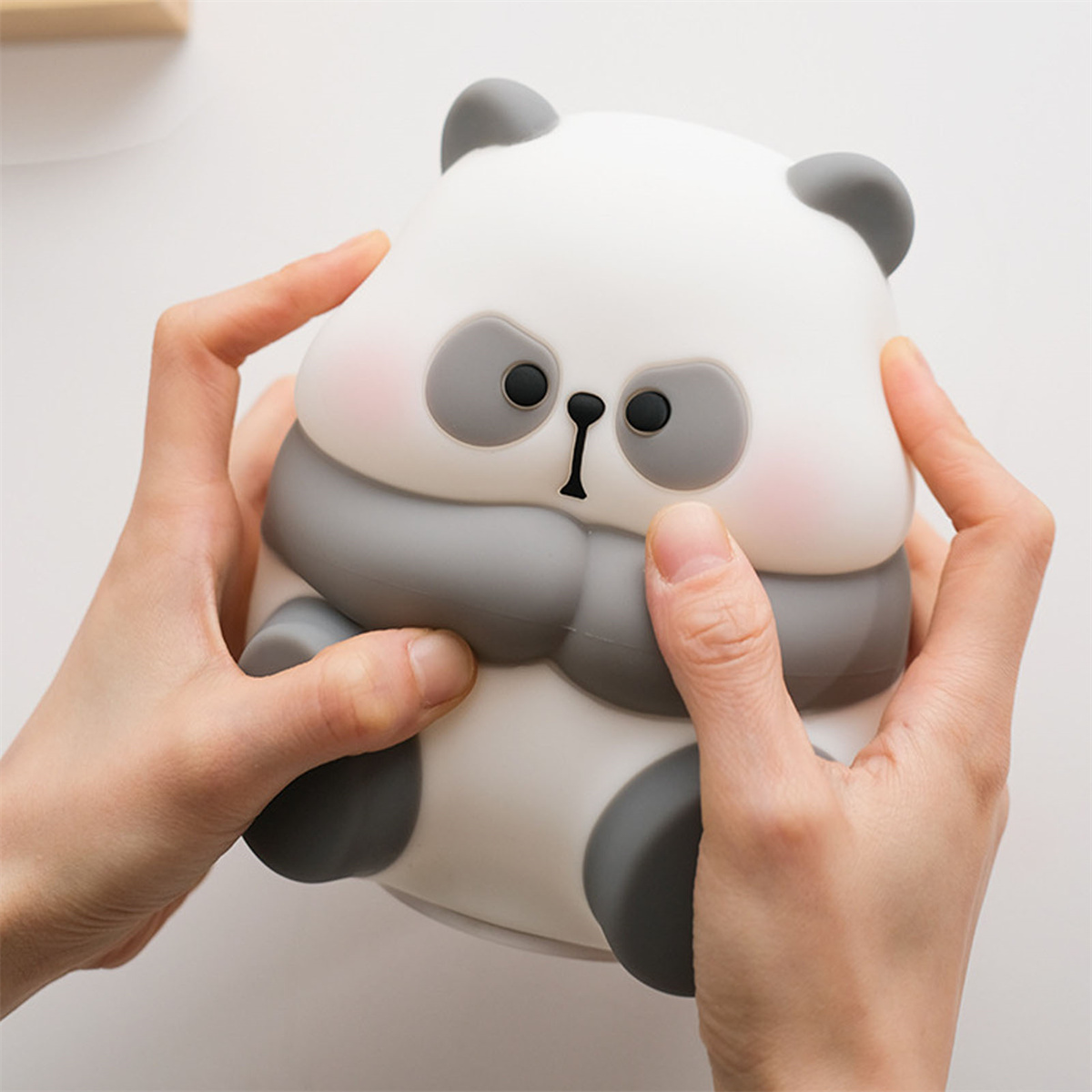 Eine weiß-graue Panda-Figur, die von zwei Händen gehalten wird. Der Panda hat graue Ohren und Augen.