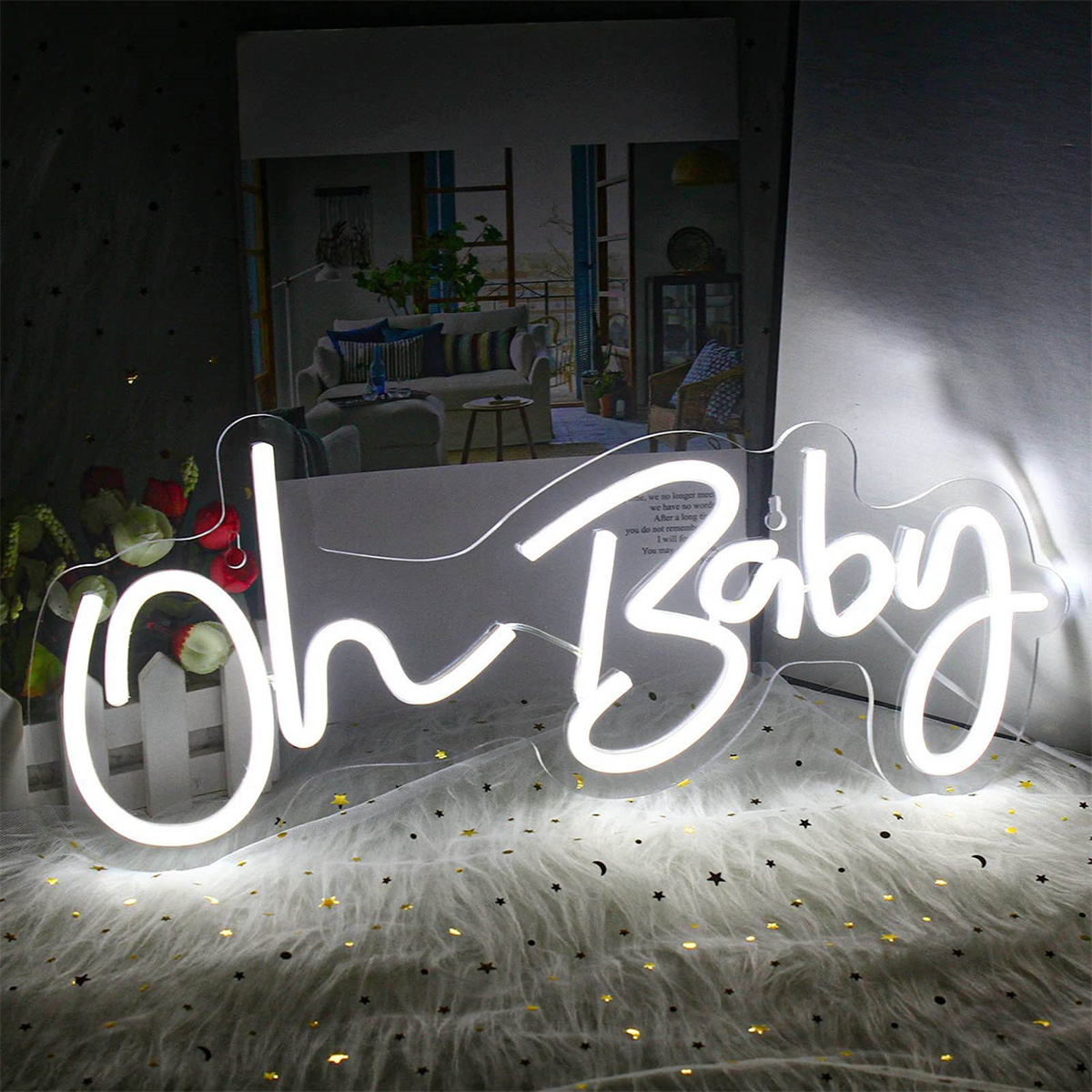 Neon-Schild mit der Aufschrift 'Oh Baby' über einer pelzigen Oberfläche, mit Blumen und einem Buch im Hintergrund.