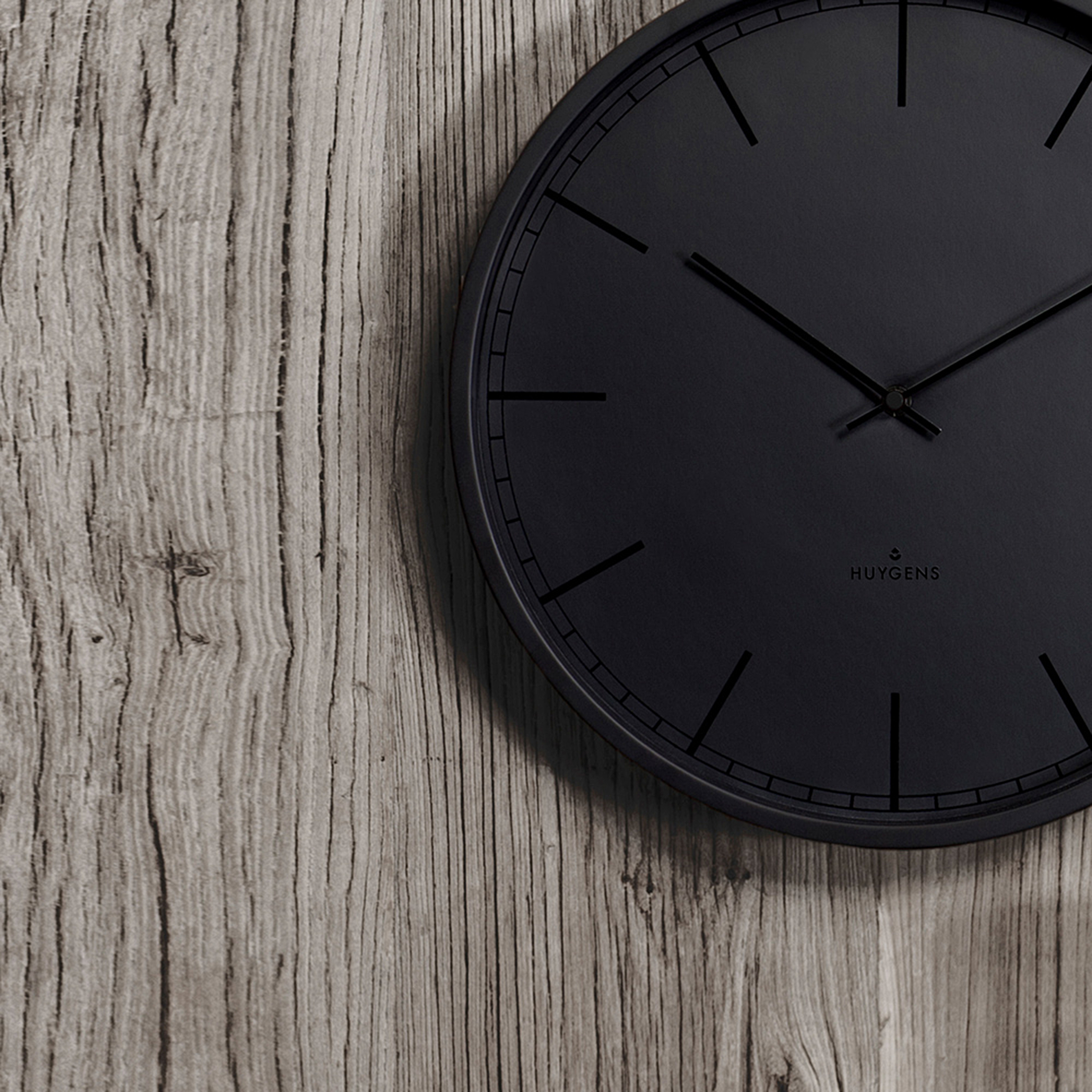 Eine schwarze Uhr auf Holzgrund mit minimalistischem Design und Logo.
