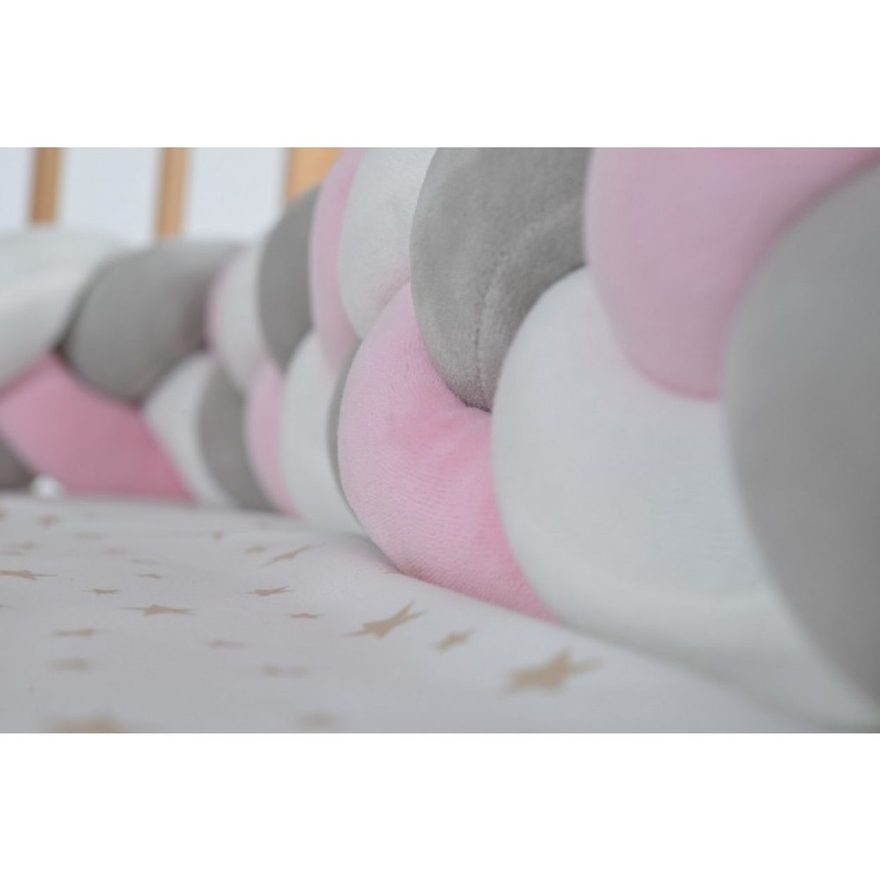 Ein Babybett-Stoßfänger, geflochtenes Design, rosa, weiß und grau.