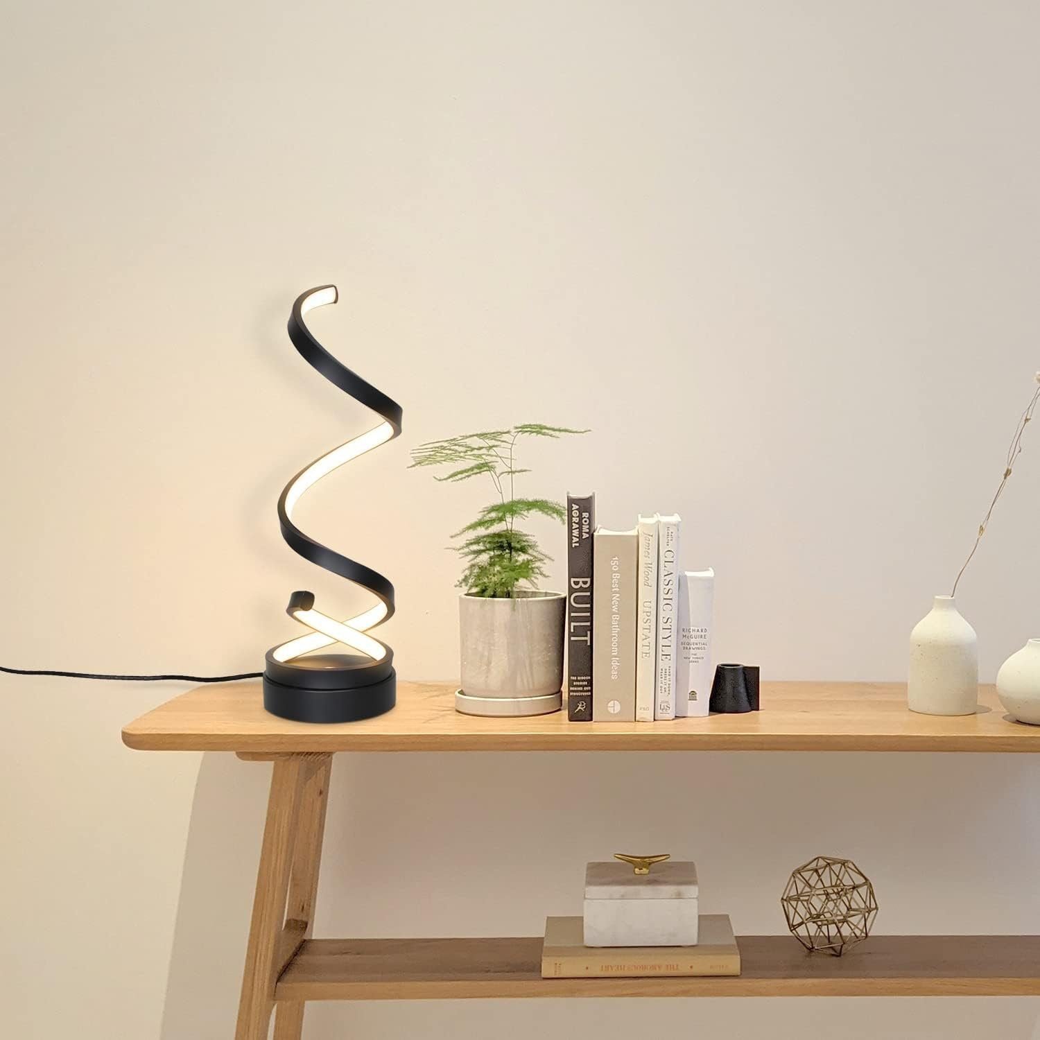 Czarna lampa spiralna na drewnianym stole z książkami, rośliną i innymi elementami dekoracyjnymi.