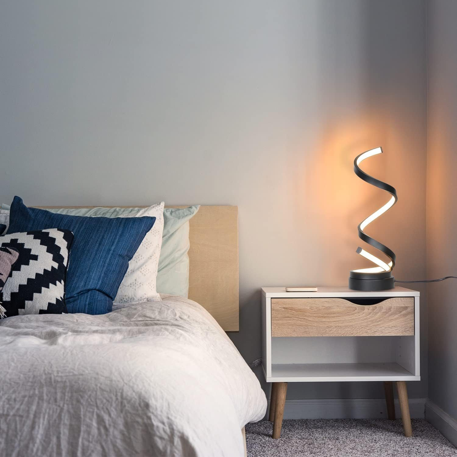 Moderne schwarz-weiße Tischlampe mit Spiraldesign auf einem Nachttisch neben einem Bett.