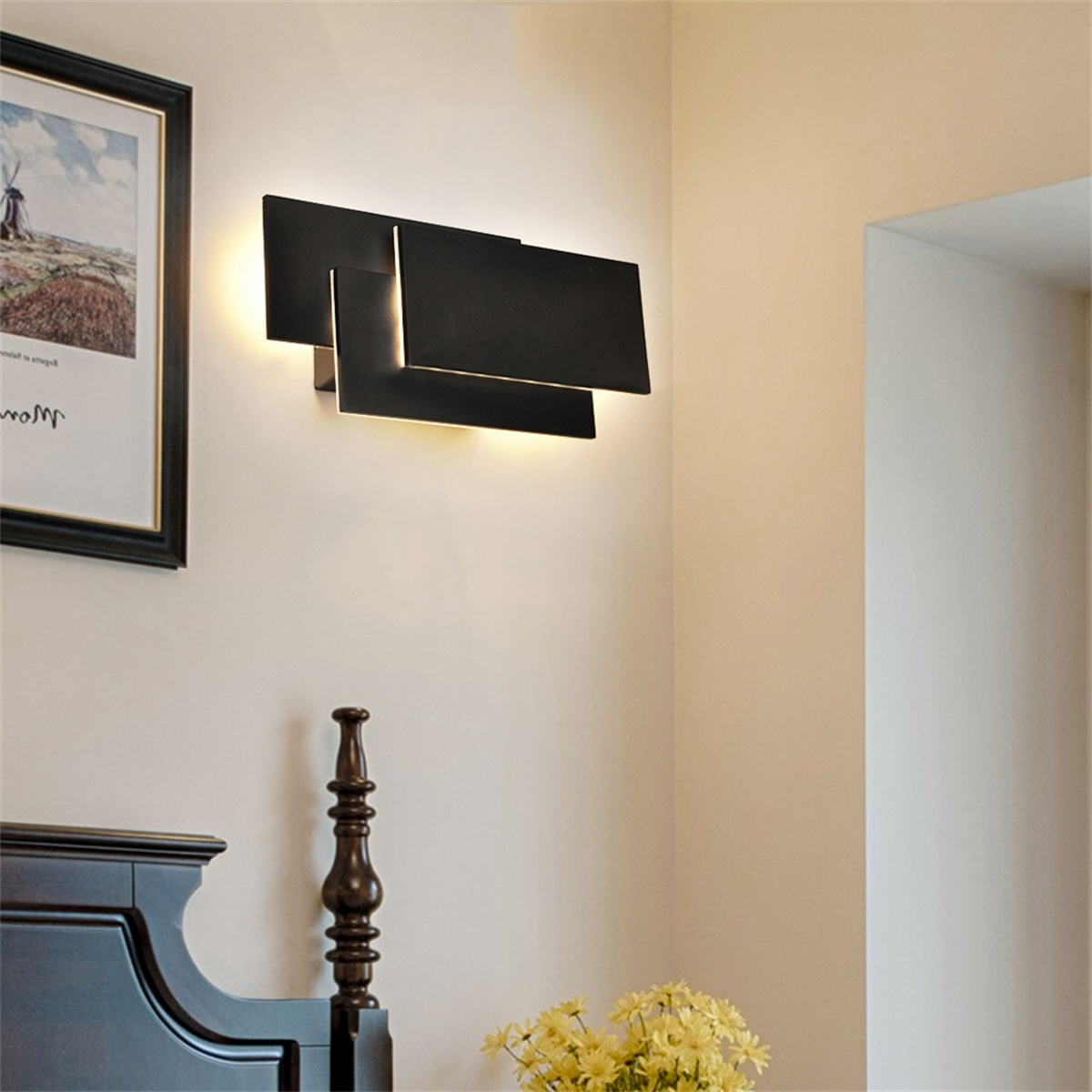Eine Wandlampe in Schwarz mit abstraktem Design und einem Bilderrahmen daneben.
