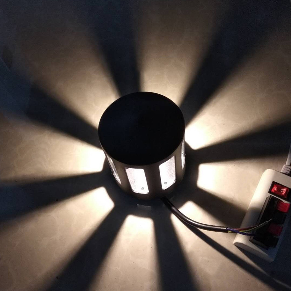 Eine runde Außenwandleuchte wirft radiale Lichtmuster und Schatten auf eine strukturierte Oberfläche.