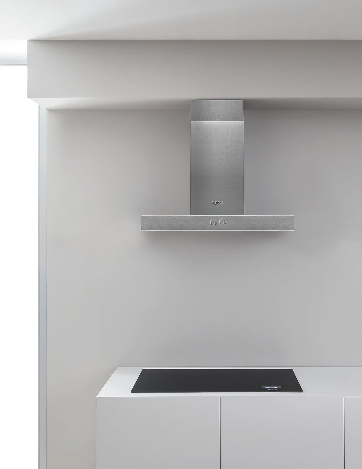 Cappa in acciaio inox montata su parete bianca sopra piano cottura nero. Design semplice e moderno.