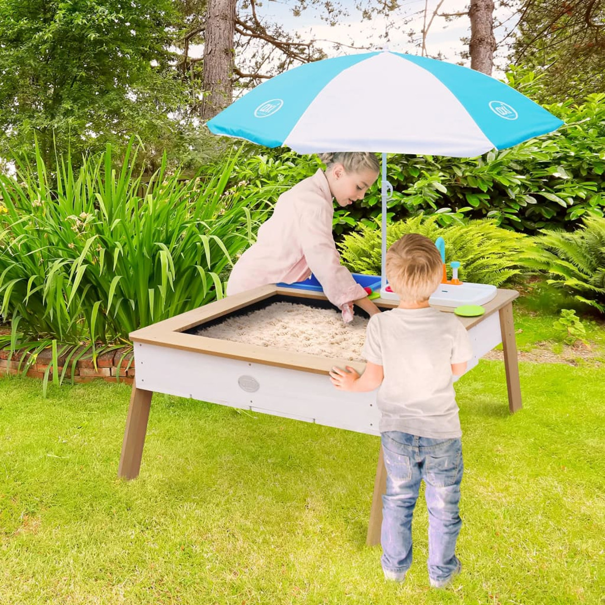 Zwei Kinder spielen in einem Sandkasten unter einem Sonnenschirm im Garten.