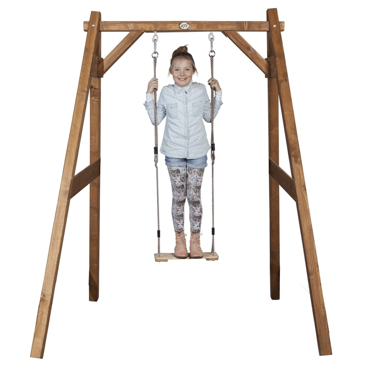 Ein junges Mädchen steht lächelnd auf einer Schaukel. Die Schaukel befindet sich in einem Holzrahmen.