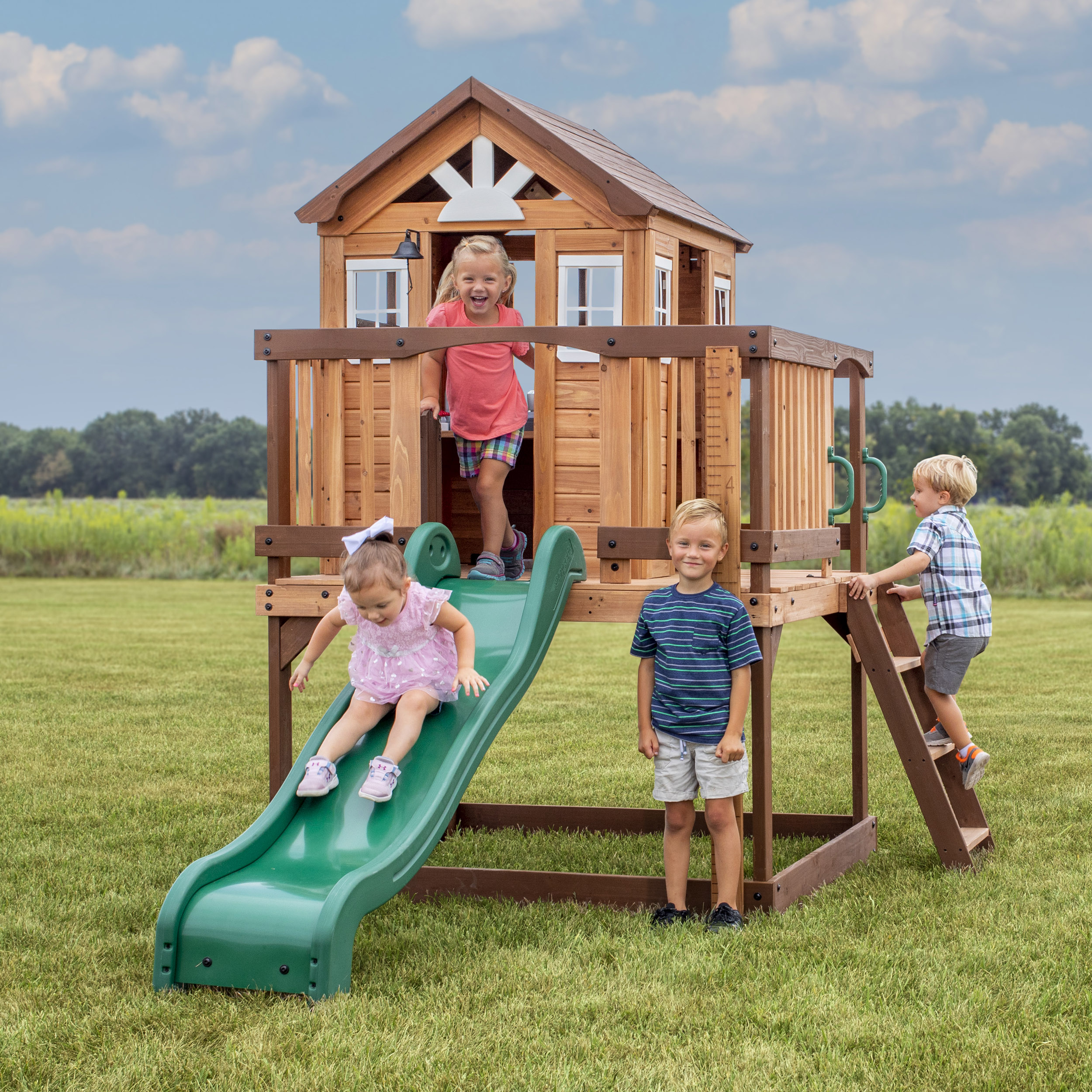 Kinder spielen auf einem Holzspielplatz mit Rutsche, Klettern und einem kleinen Haus.