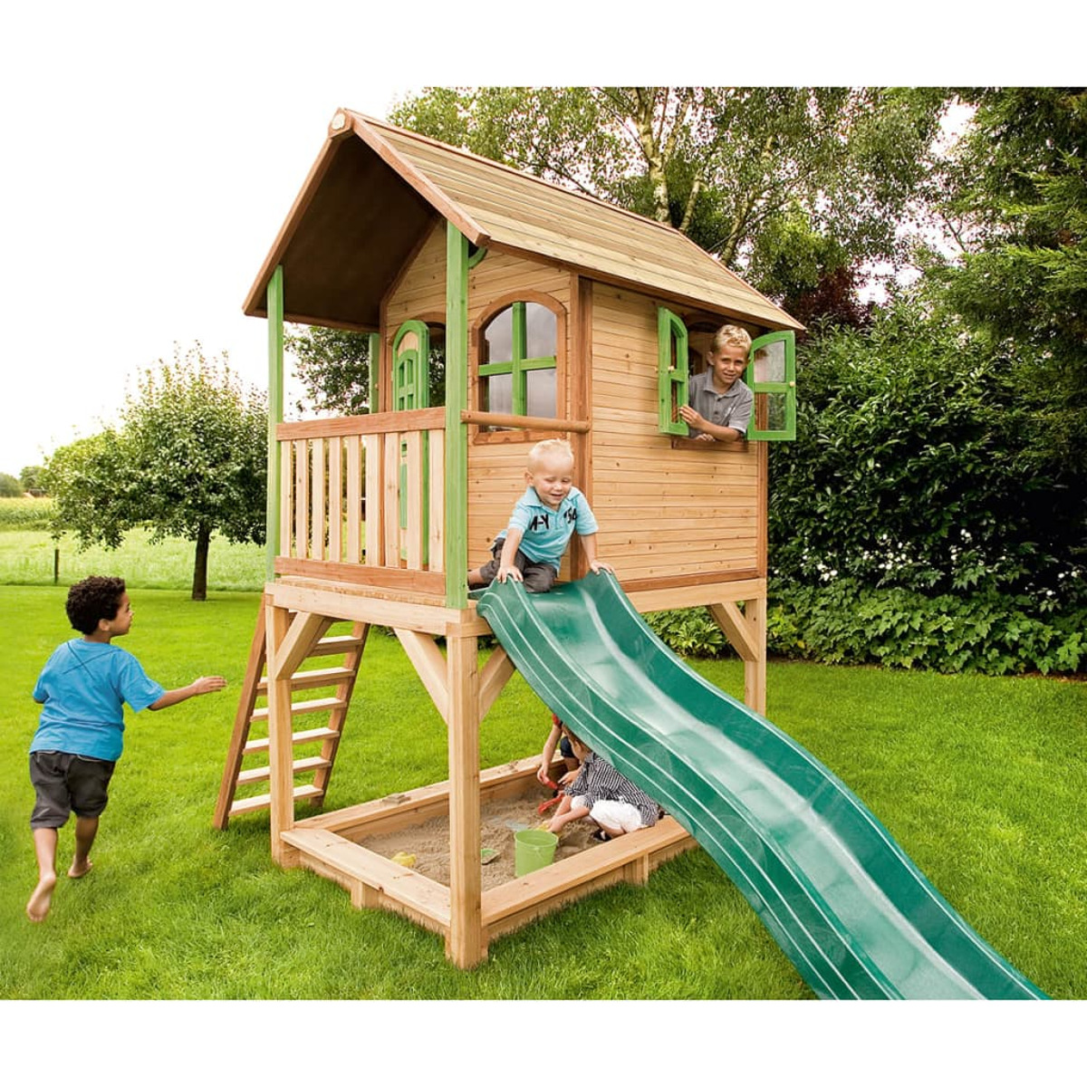 Spielhaus aus Holz mit Rutsche, Leiter und zwei spielenden Kindern. Grüne Rutsche und Gras im Hintergrund.