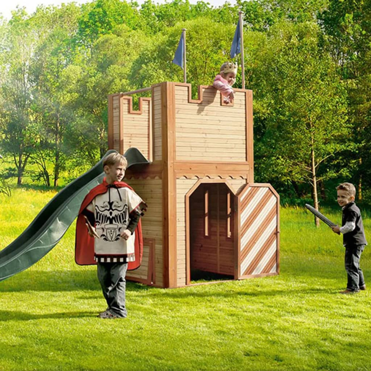 Kinder spielen in einem Holzschloss mit Rutsche und zwei Fahnen auf einer grünen Wiese.