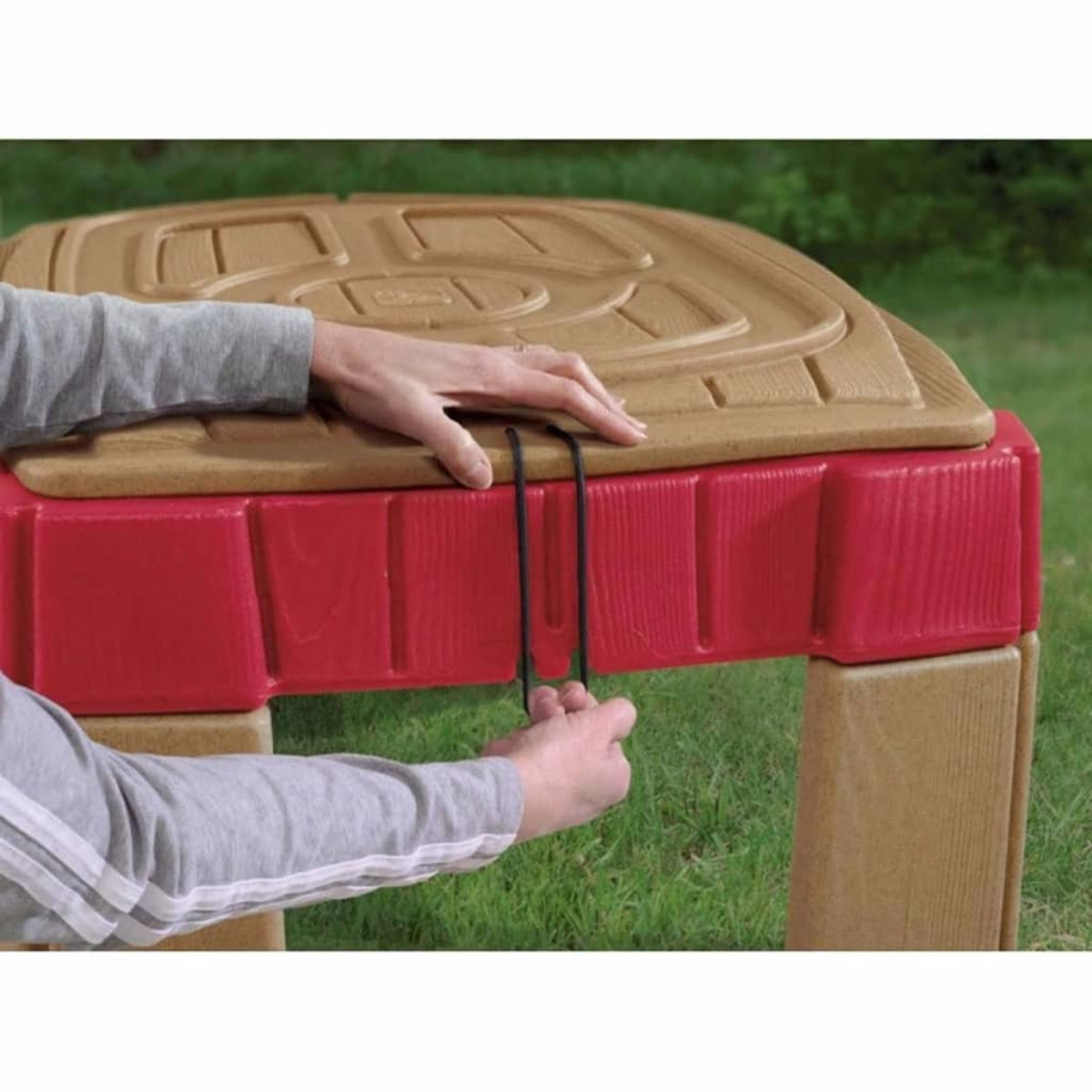 Hände einer Person, die einen roten und hellbraunen Kunststoff-Spielplatz sichern.