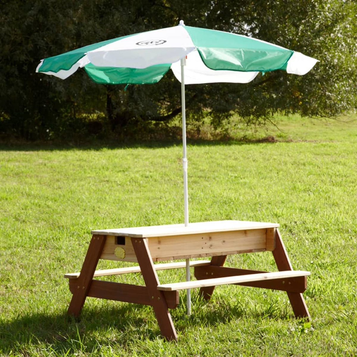 Picknicktisch mit grün-weißem Schirm. Auf Gras. Baum im Hintergrund.