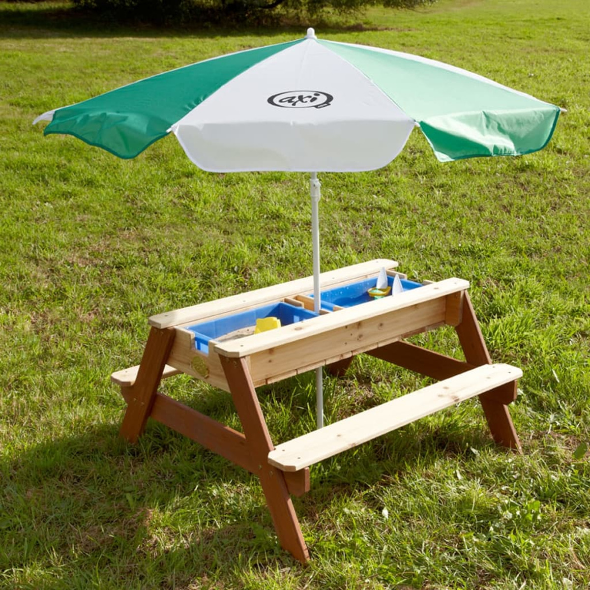 Ein Picknicktisch aus Holz mit einem grün-weißen Sonnenschirm. Auf einer Wiese.