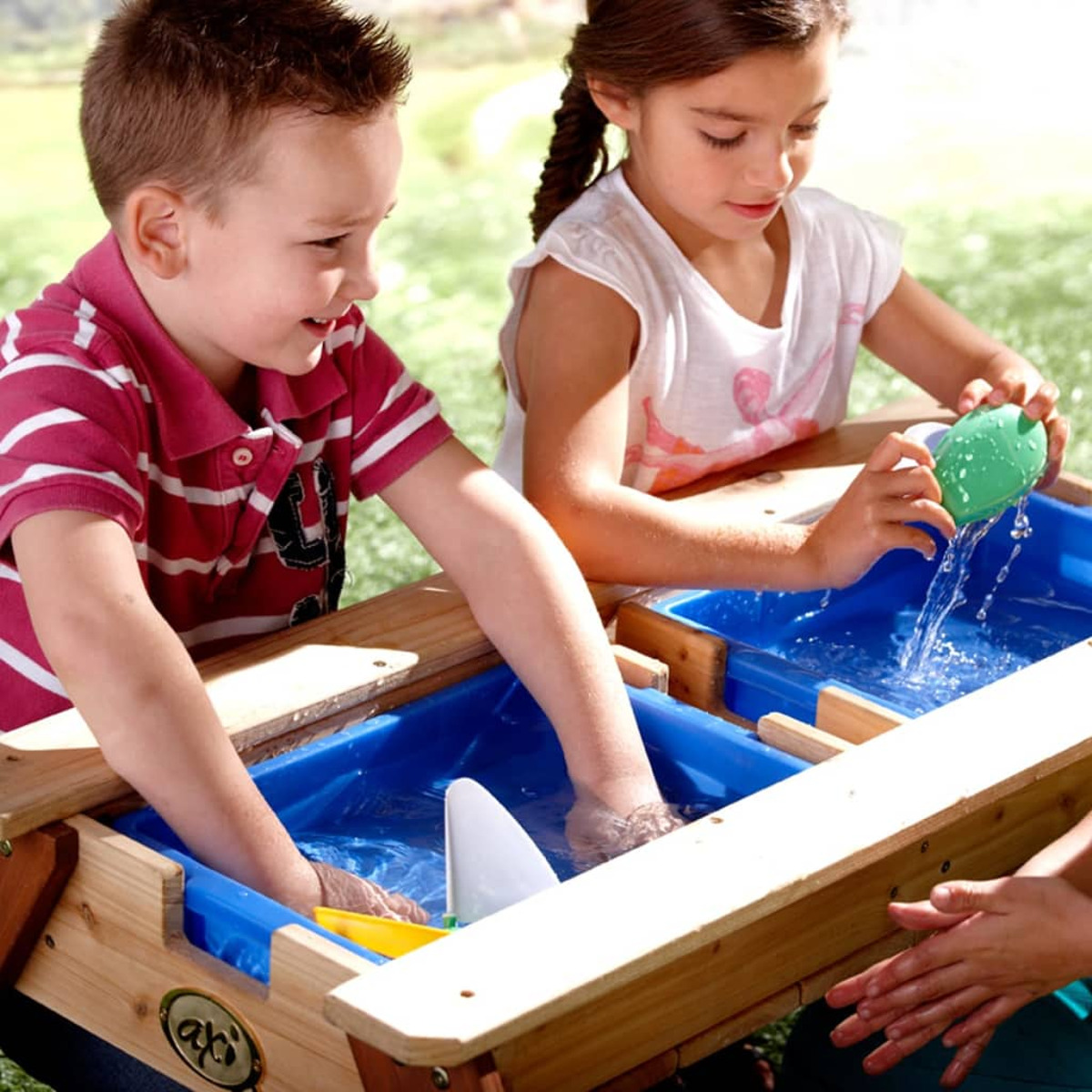 Zwei Kinder spielen draußen mit Spielzeug an einem Wassertisch.