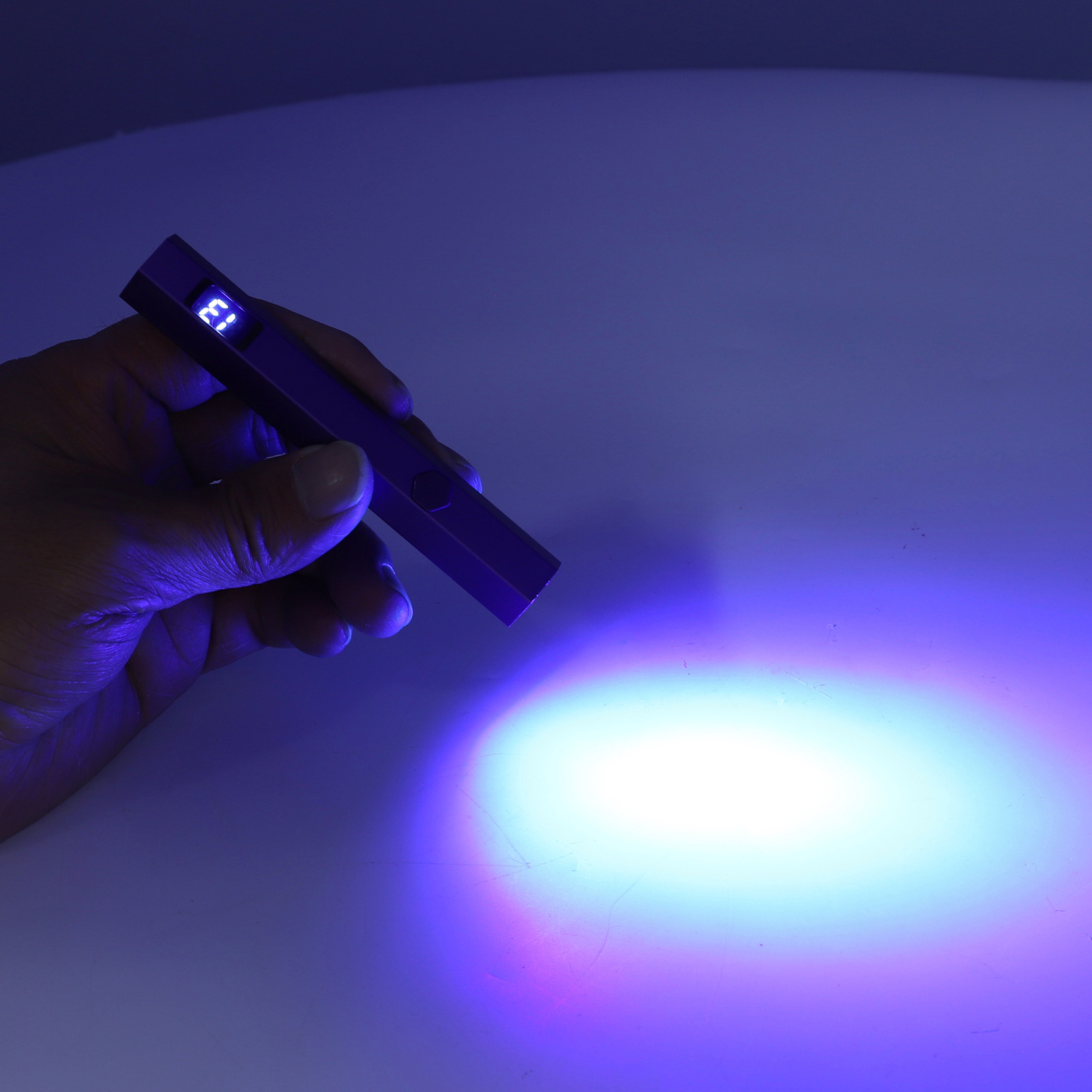 Hand hält einen violetten UV-Lichtstift, der eine Oberfläche mit blauem Glanz beleuchtet.