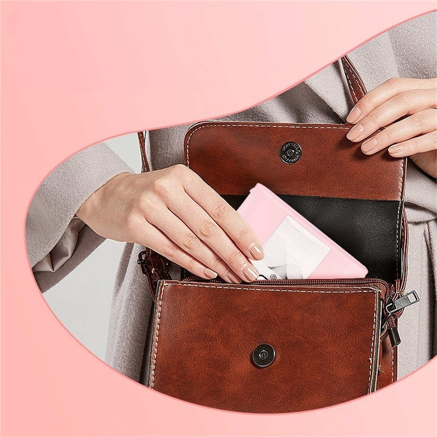 Eine Hand öffnet eine braune Ledertasche und hält eine rosa Hülle.