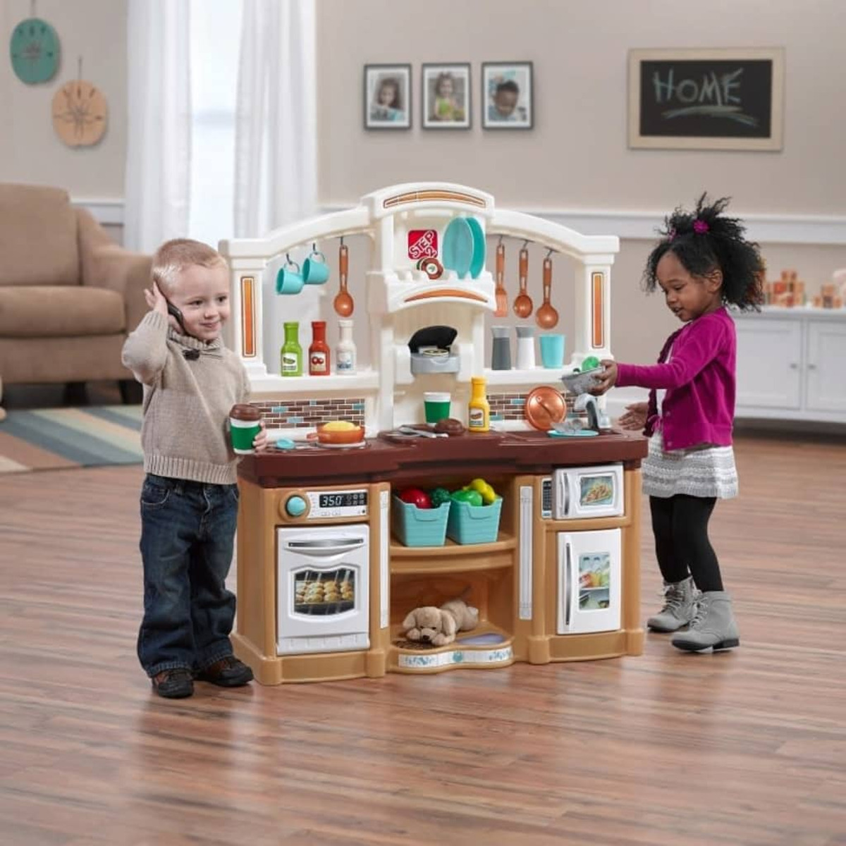 Due bambini giocano con un set di cucina giocattolo. Un bambino è al telefono, una bambina cucina.