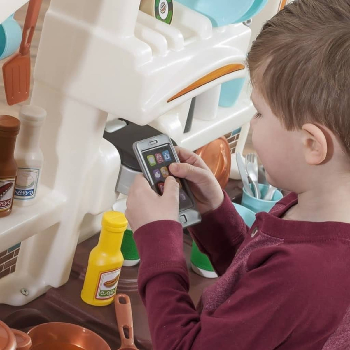 Un ragazzino gioca con una cucina giocattolo, tenendo un telefono vicino alle caratteristiche del gioco.