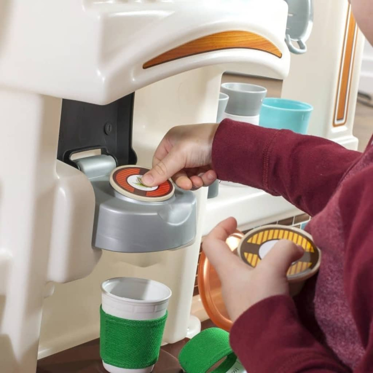 Un bambino inserisce una cialda di caffè in una macchina per il caffè giocattolo. Tazze e cialde aggiuntive sono visibili.