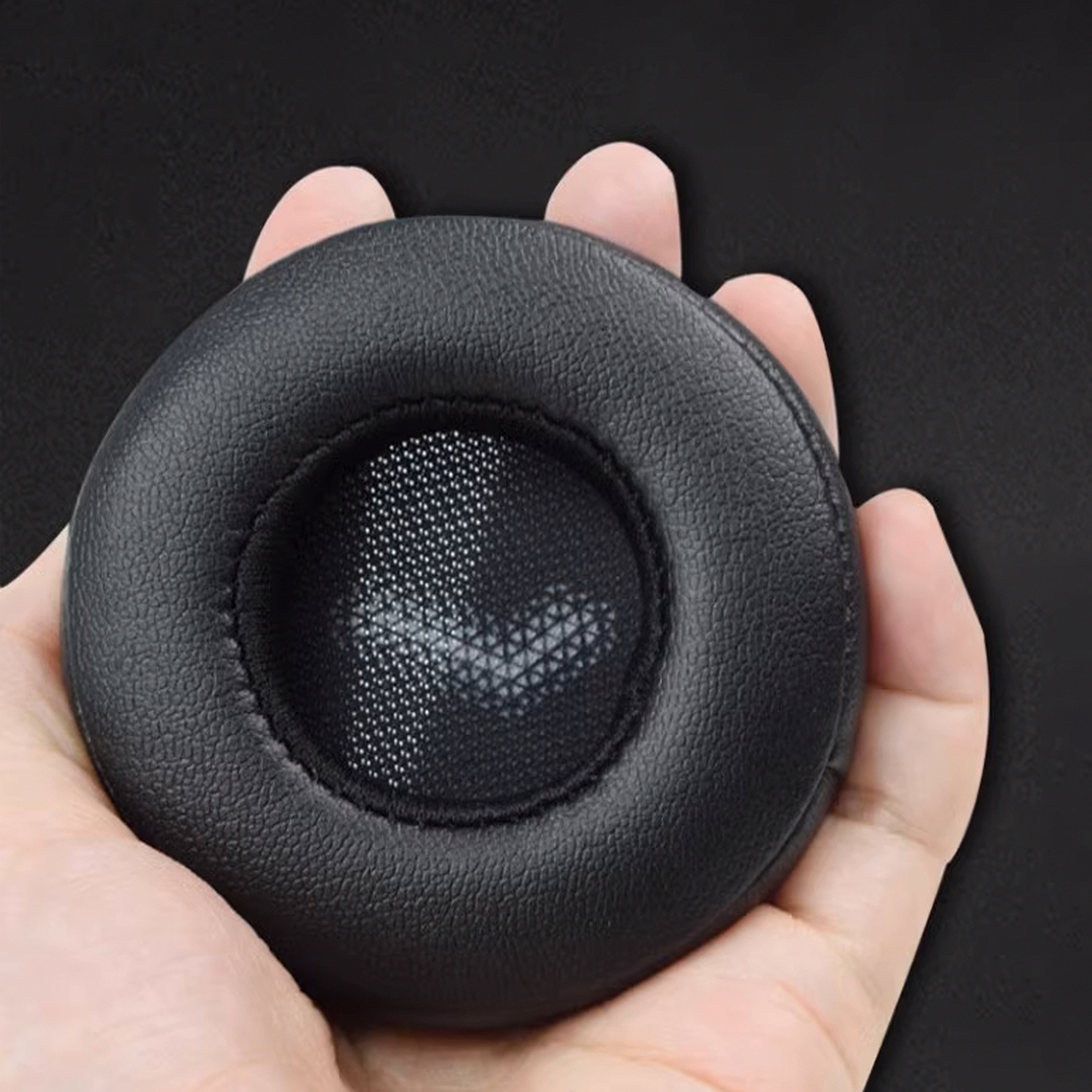 Ręka trzyma czarną, okrągłą poduszkę do słuchawek z siatkowym środkiem.