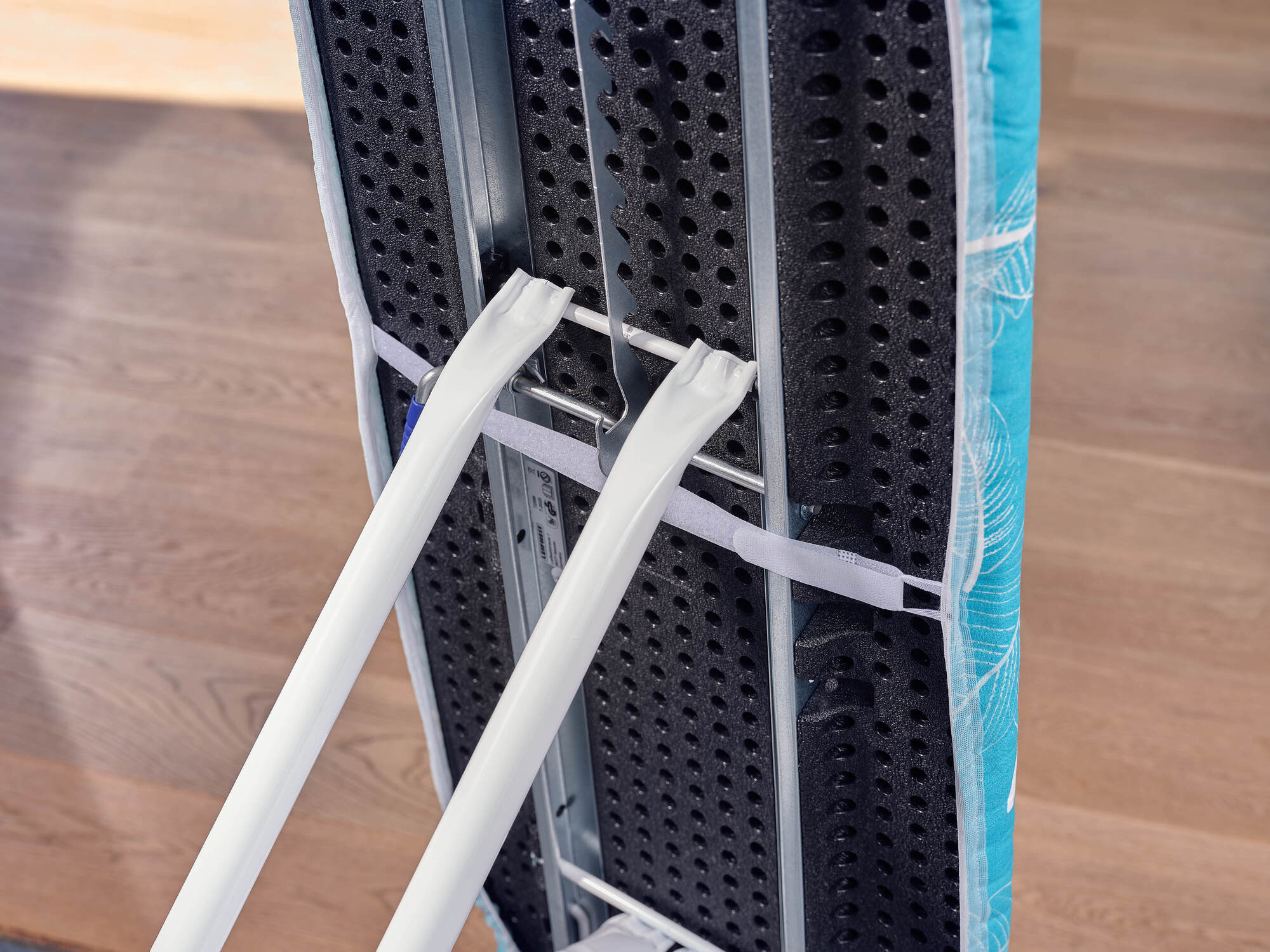 Deska do prasowania z niebieskim kwiatowym pokrowcem, białymi nogami i paskami.