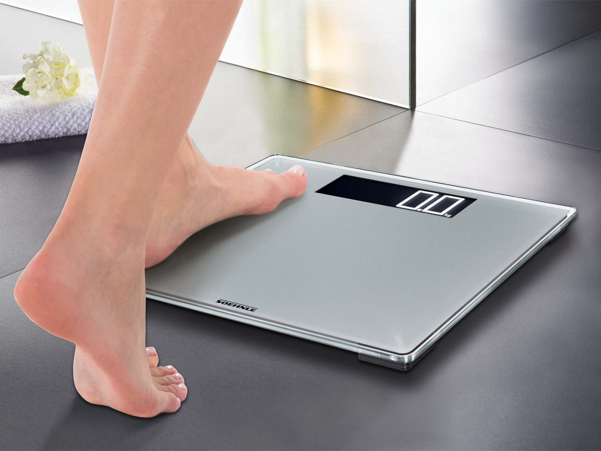 Stopa na wadze cyfrowej z wyświetlaczem '0.0', w otoczeniu łazienki.