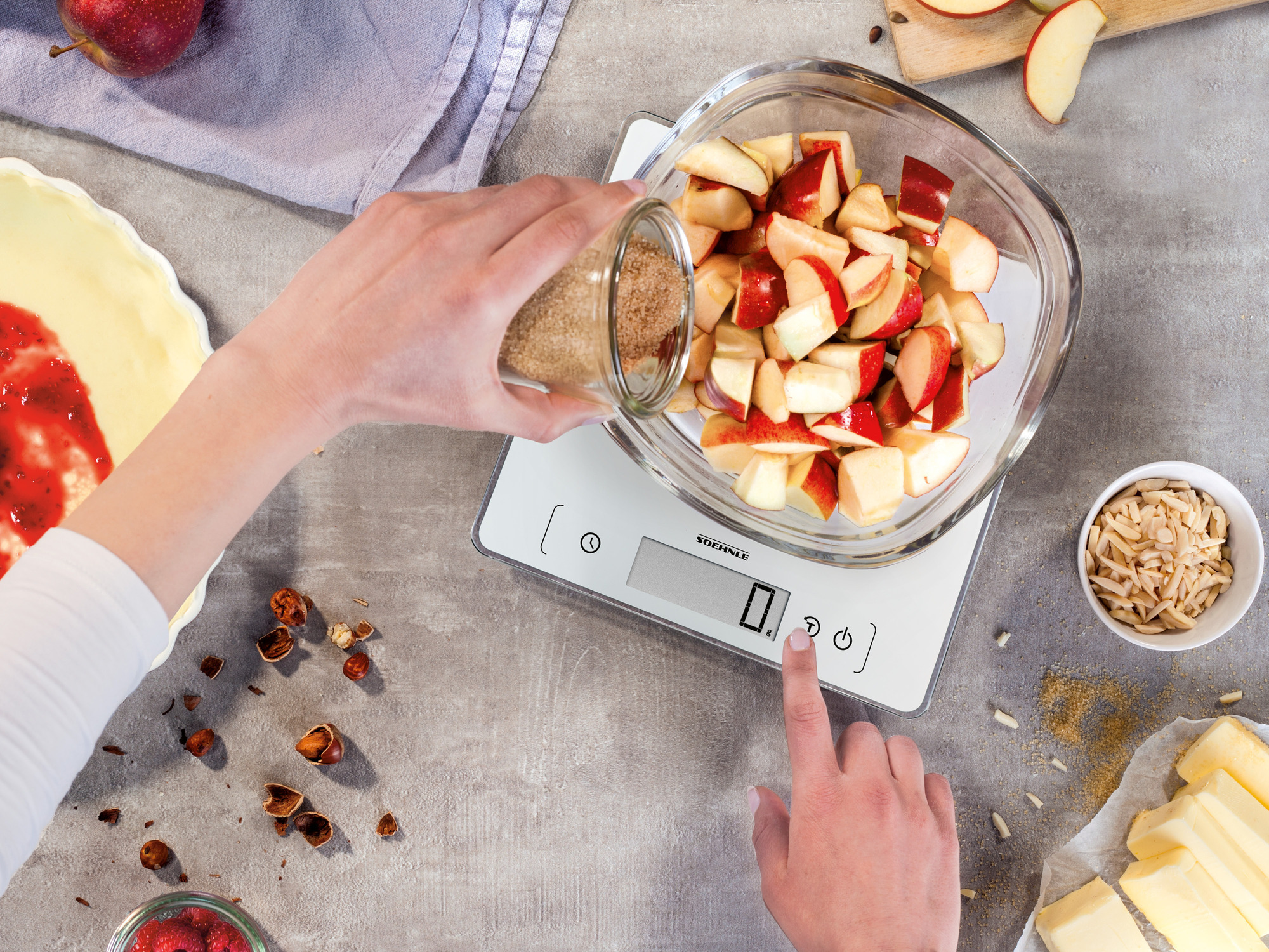 Dłonie wsypujące brązowy cukier do miski z pokrojonymi jabłkami na wadze.