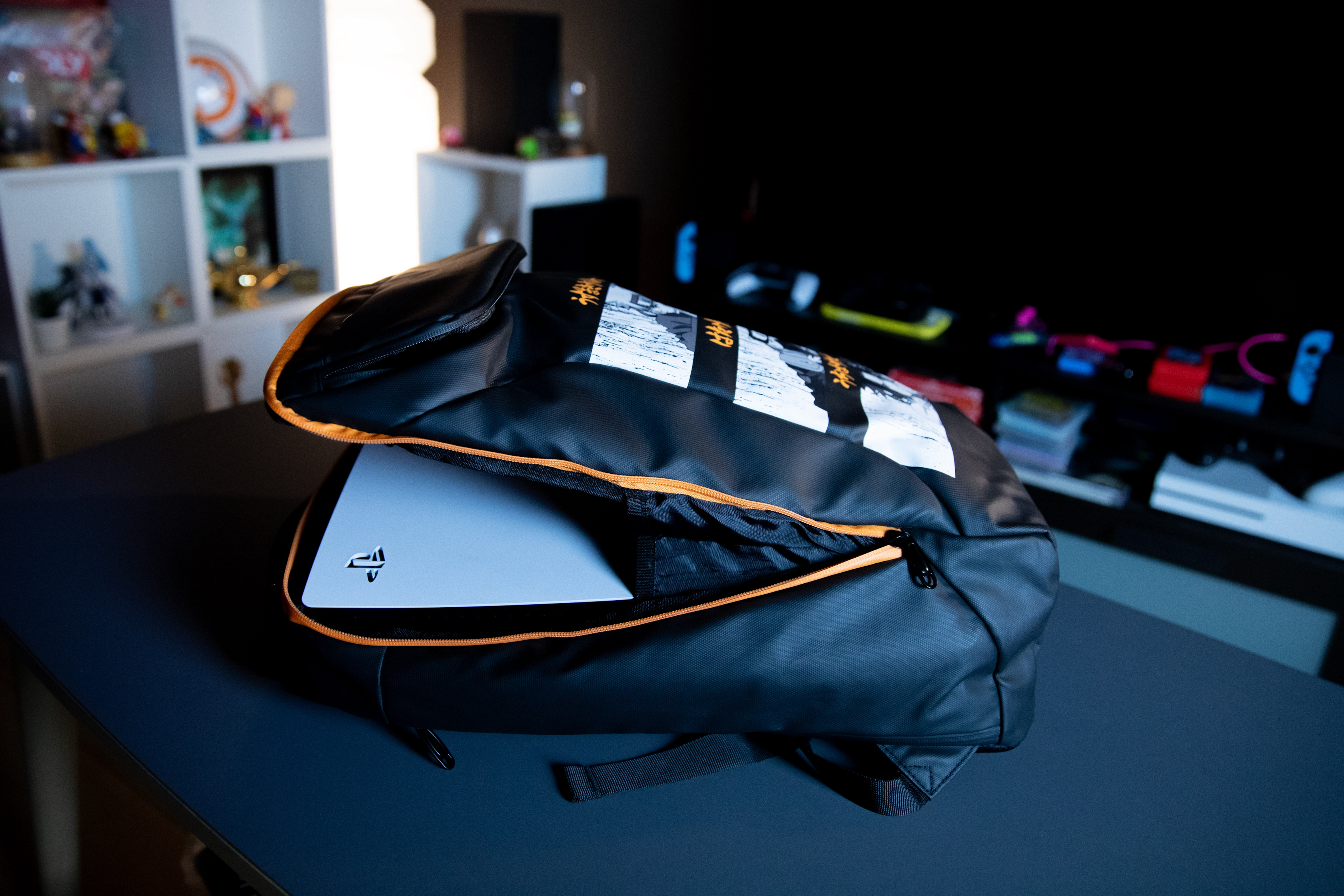 Ein offener schwarzer Rucksack mit orangefarbenem Reißverschluss. Eine Playstation 5 ist drin.