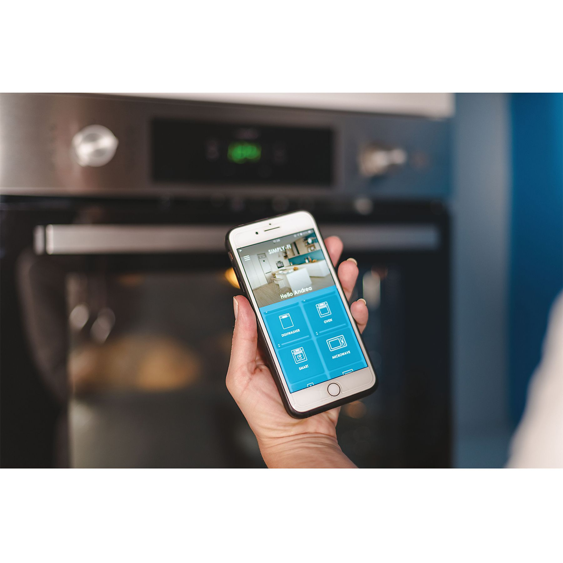 Mano che tiene uno smartphone davanti a un forno. Il telefono mostra un'interfaccia app.