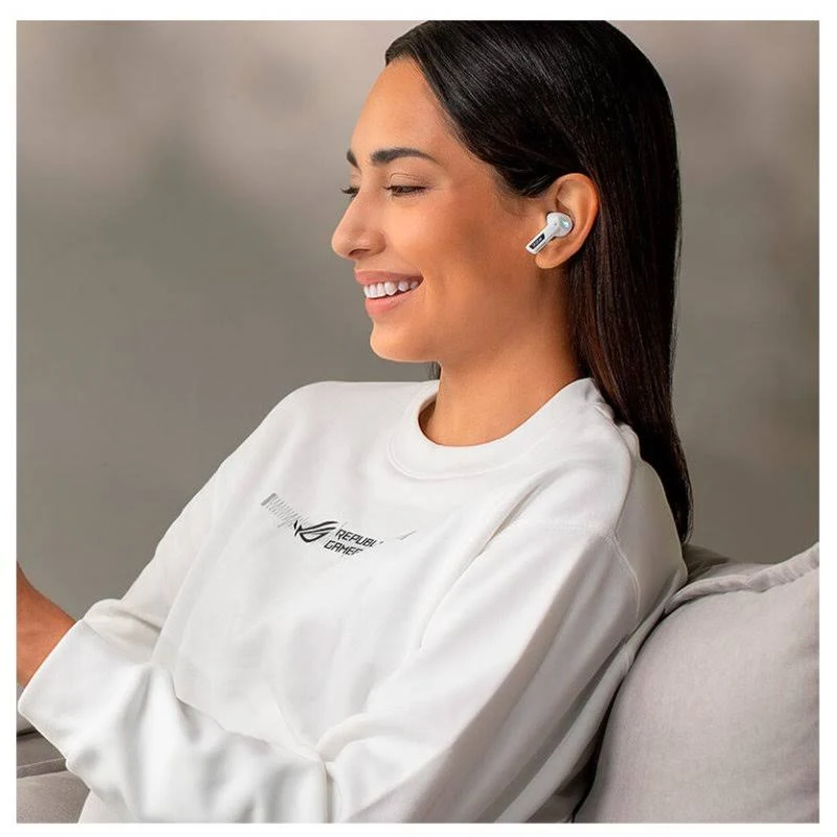 Una donna con auricolari nell'orecchio, con una camicia bianca e sorridente, con uno sfondo grigio.
