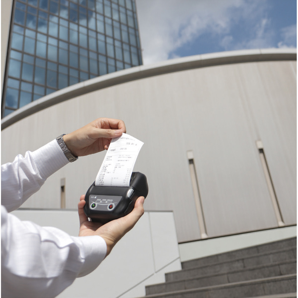 A person holding a receipt coming out of a black portable printer, outdoors.