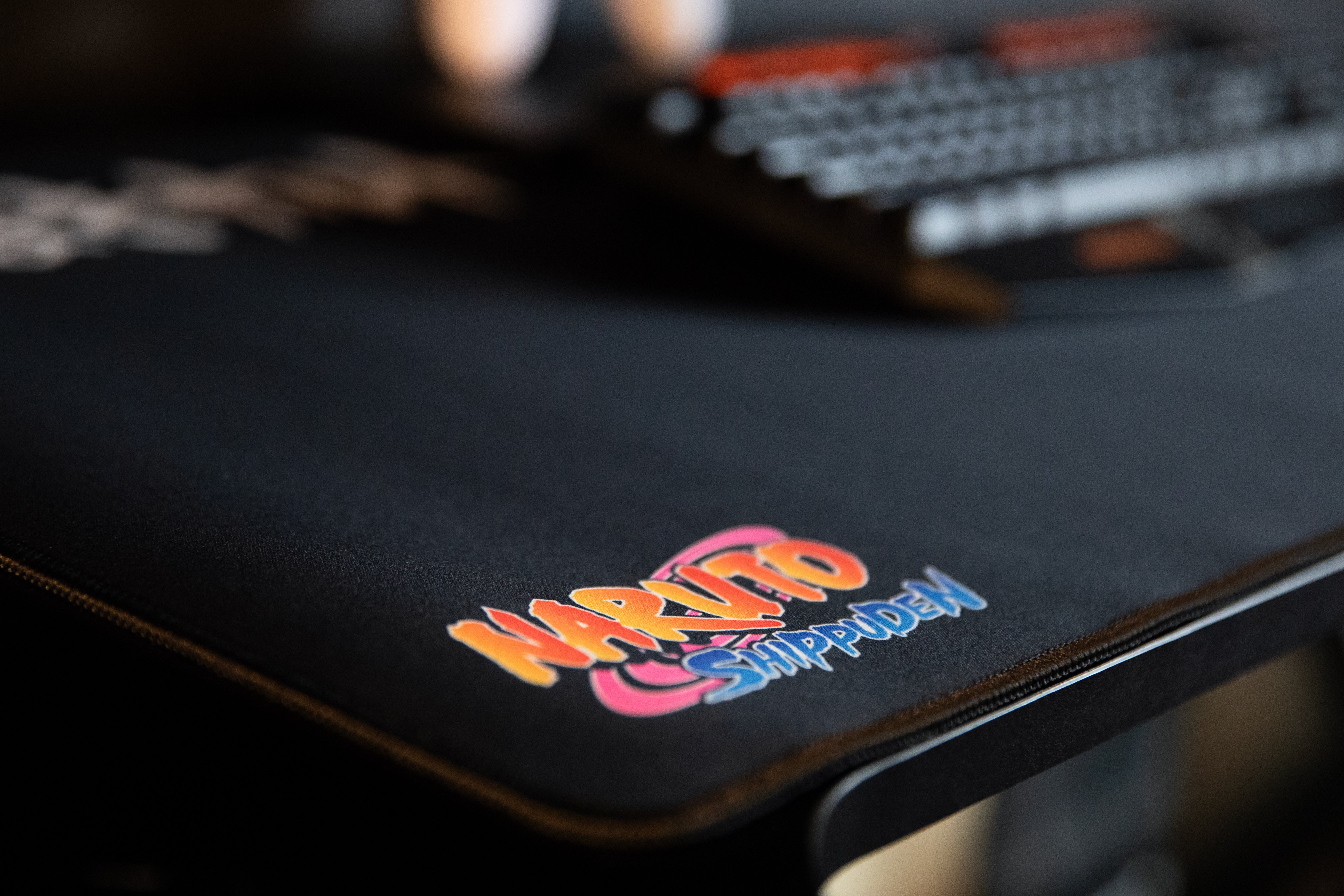 Alfombrilla de ratón negra con el logo de Naruto Shippuden. Teclado en el fondo.