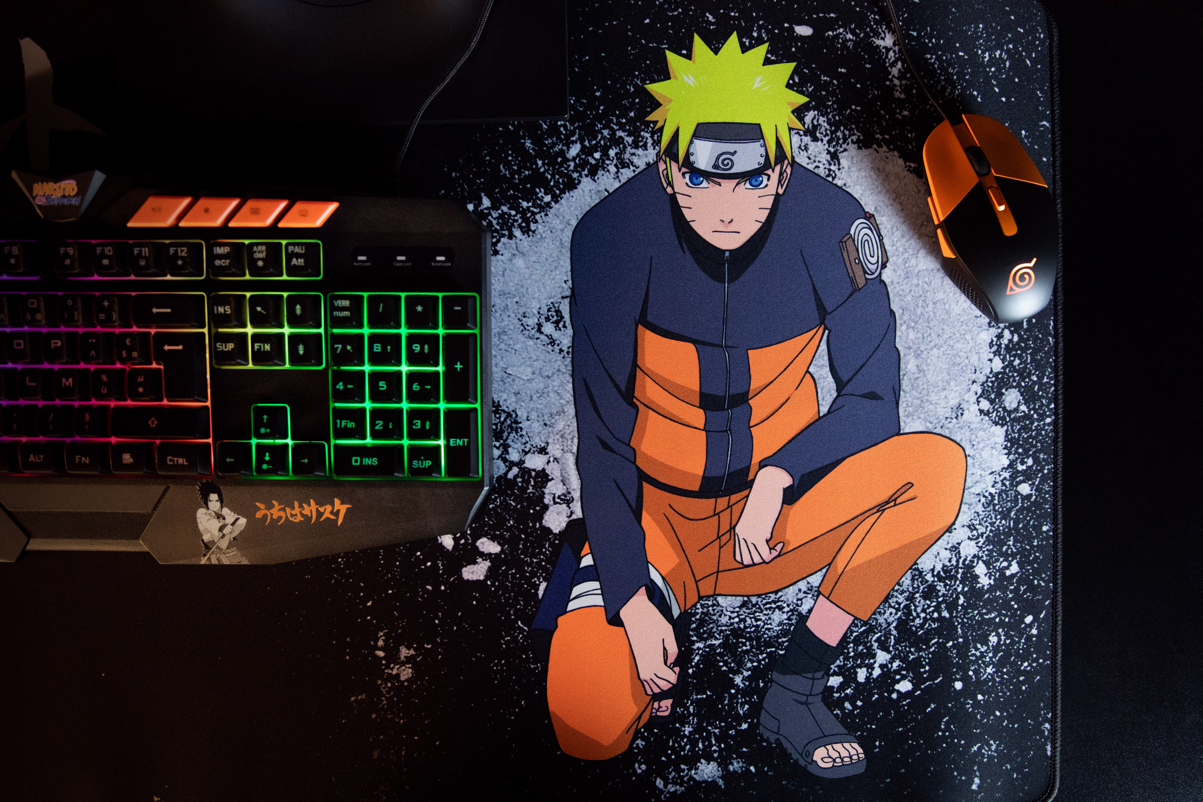 Alfombrilla de ratón de Naruto con teclado y ratón. El personaje de Naruto está sentado en la almohadilla. Fondo oscuro.
