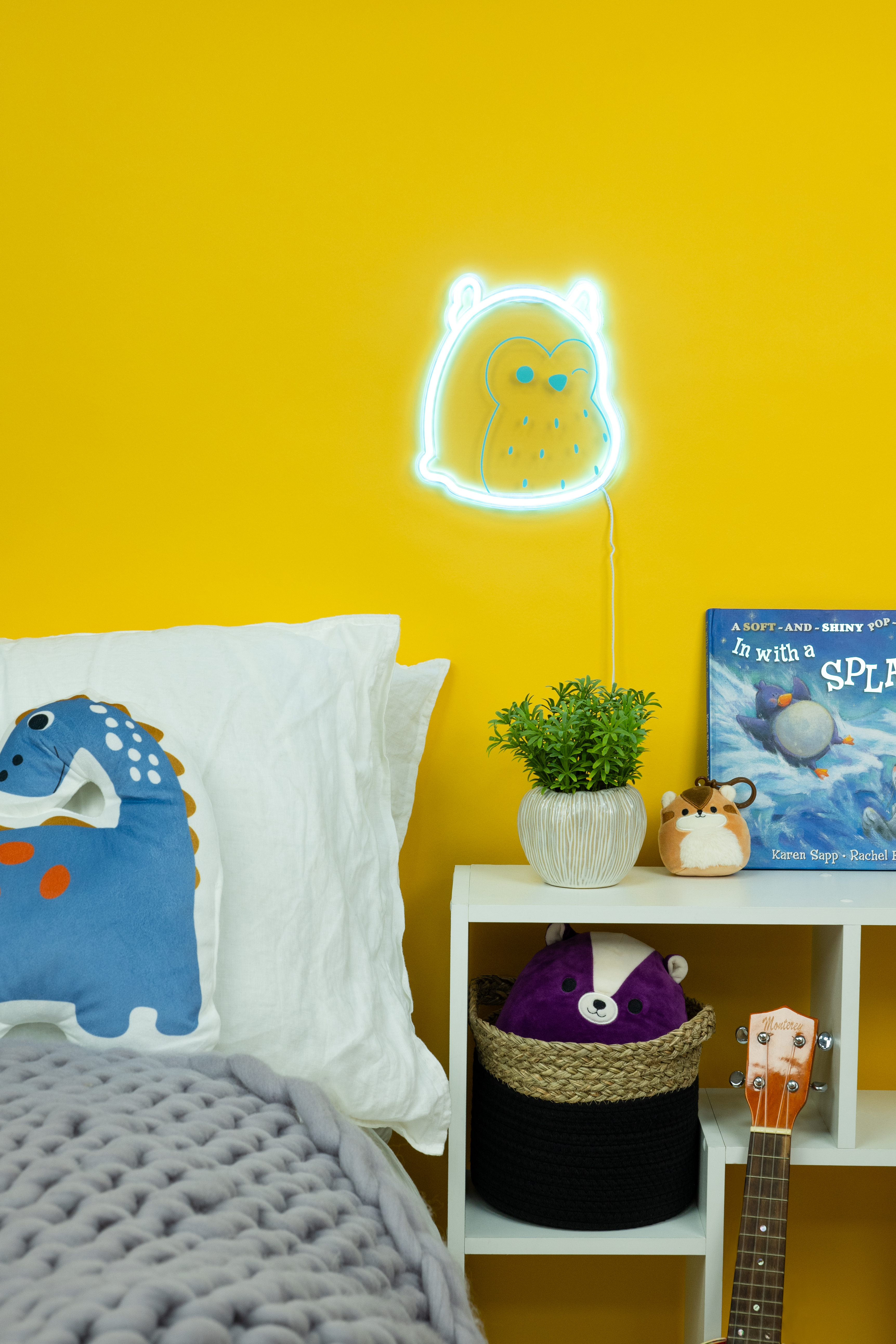 Een slaapkamerscène met een uil neonlicht, bed, plank en planten. Gele muur, gezellig, warme verlichting.