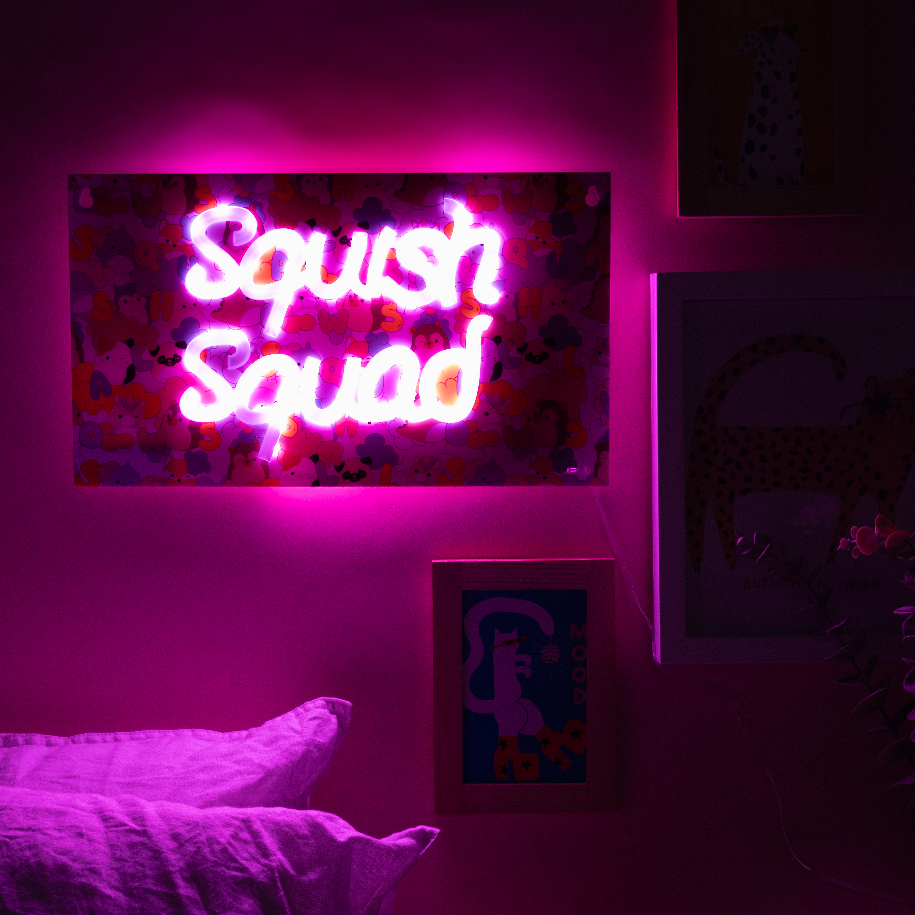 Neonbord met 'Squish Squad' in een roze kamer met kunstwerken en kussens, met roze verlichting.