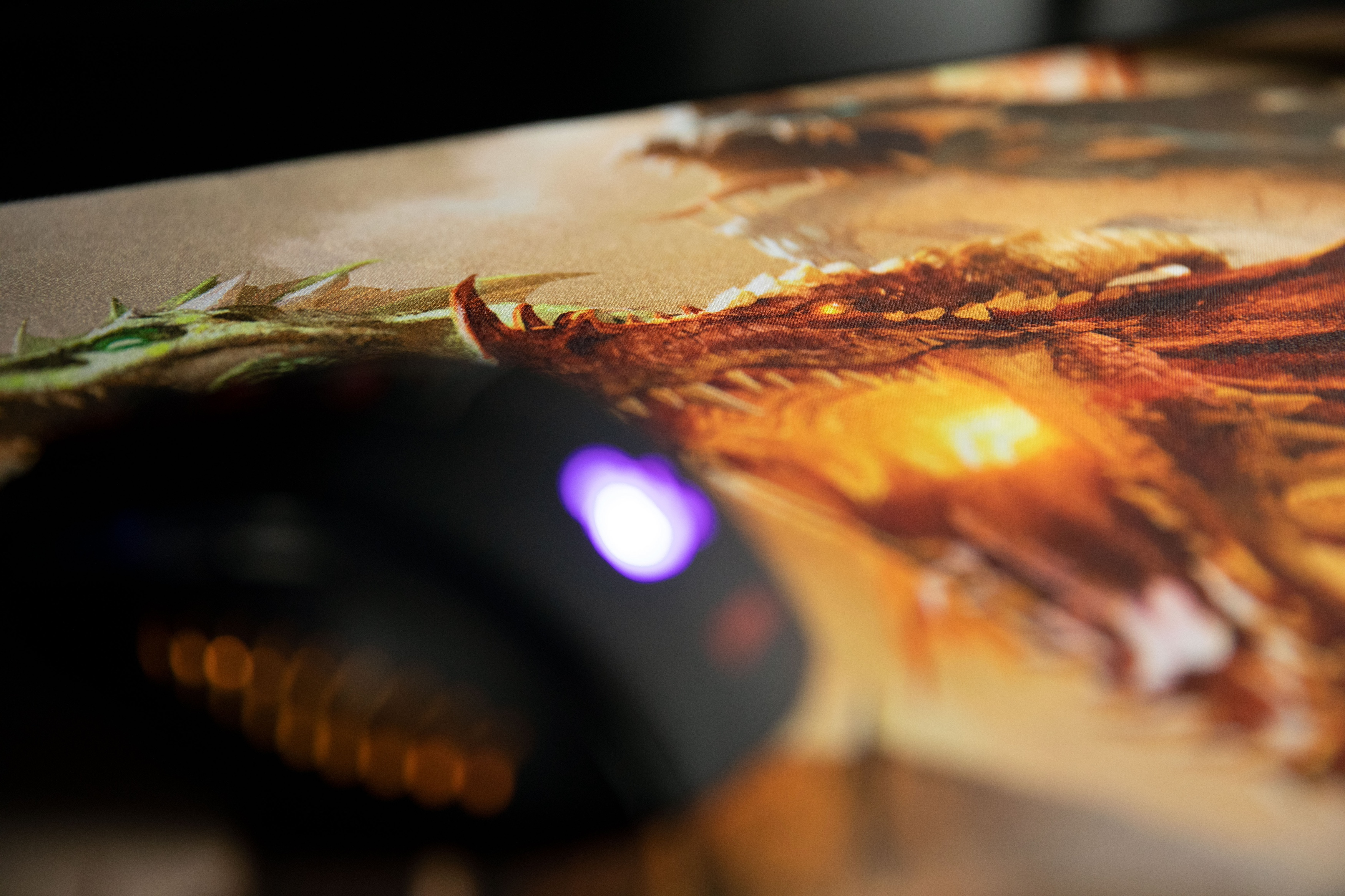 Mysz na podkładce z wizerunkiem smoka. Mysz jest czarna, a smok czerwonobrązowy z pomarańczowymi akcentami.